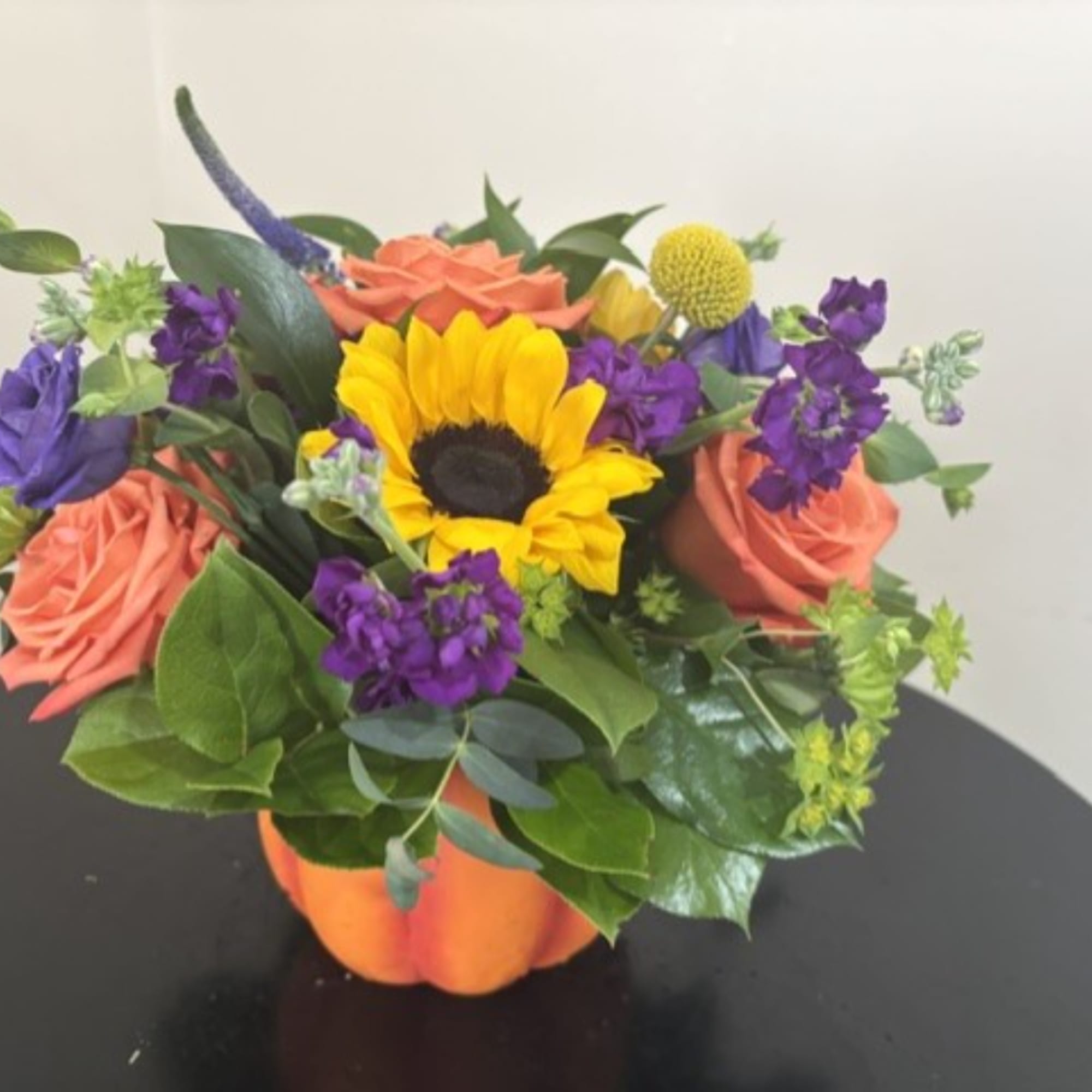 Bouquet with a sunflower, coral roses, and purple flowers in an orange pumpkin container