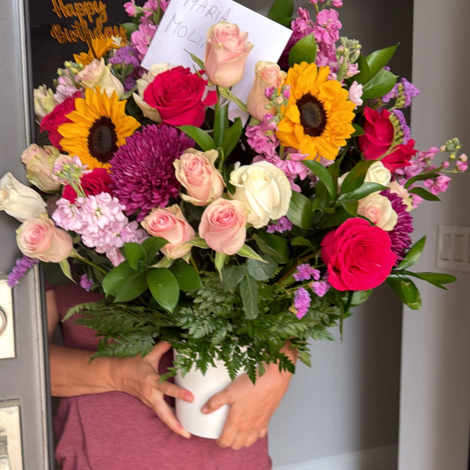 Mixed bouquet of roses, sunflowers, and mums in a white vase