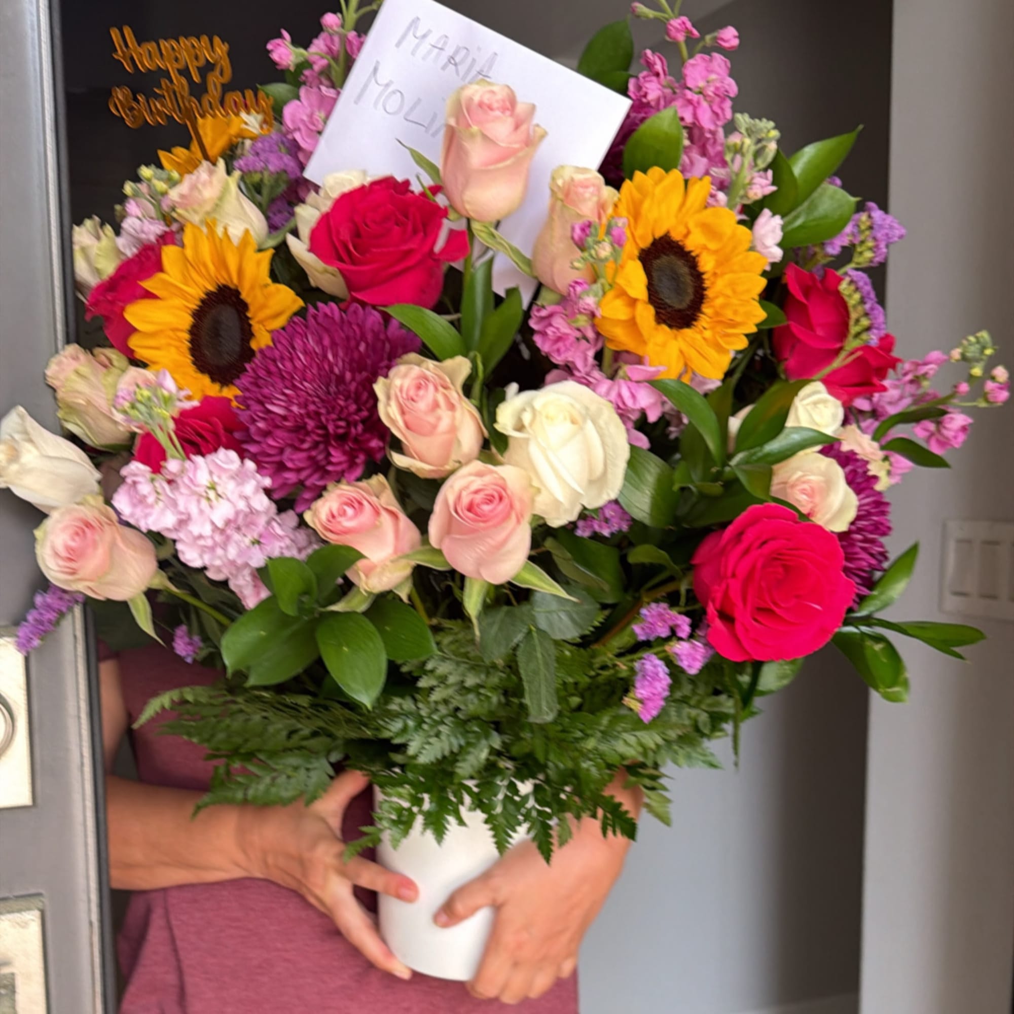 Mixed bouquet of roses, sunflowers, and purple blooms in a white vase