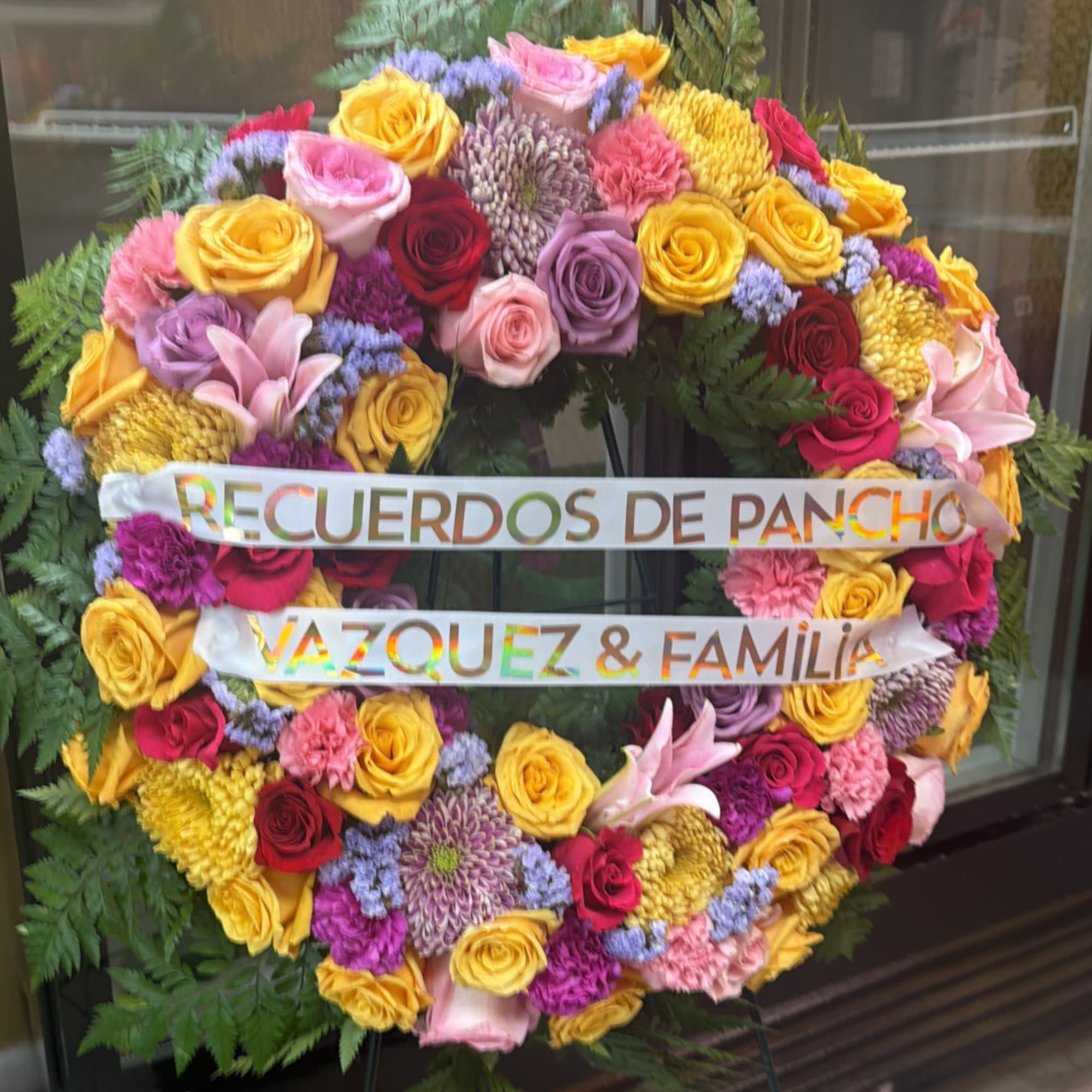 Large floral wreath with colorful roses and ribbons reading "RECUERDOS DE PANCHO"