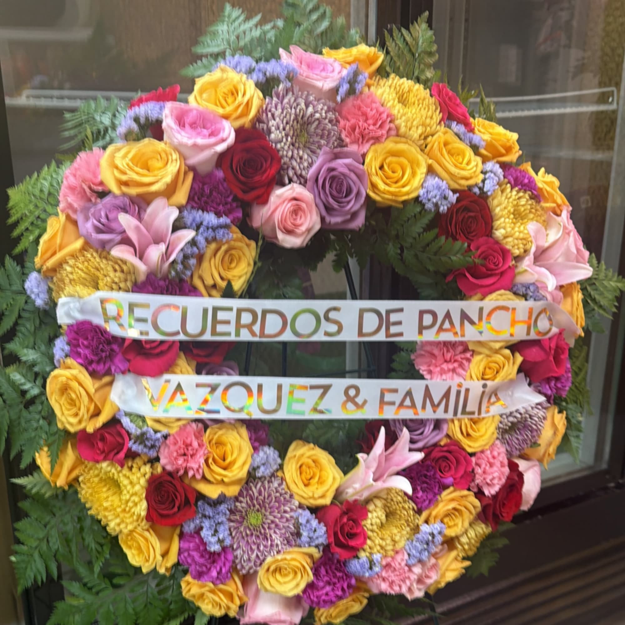 Large floral wreath with roses, lilies, and ribbon tribute text