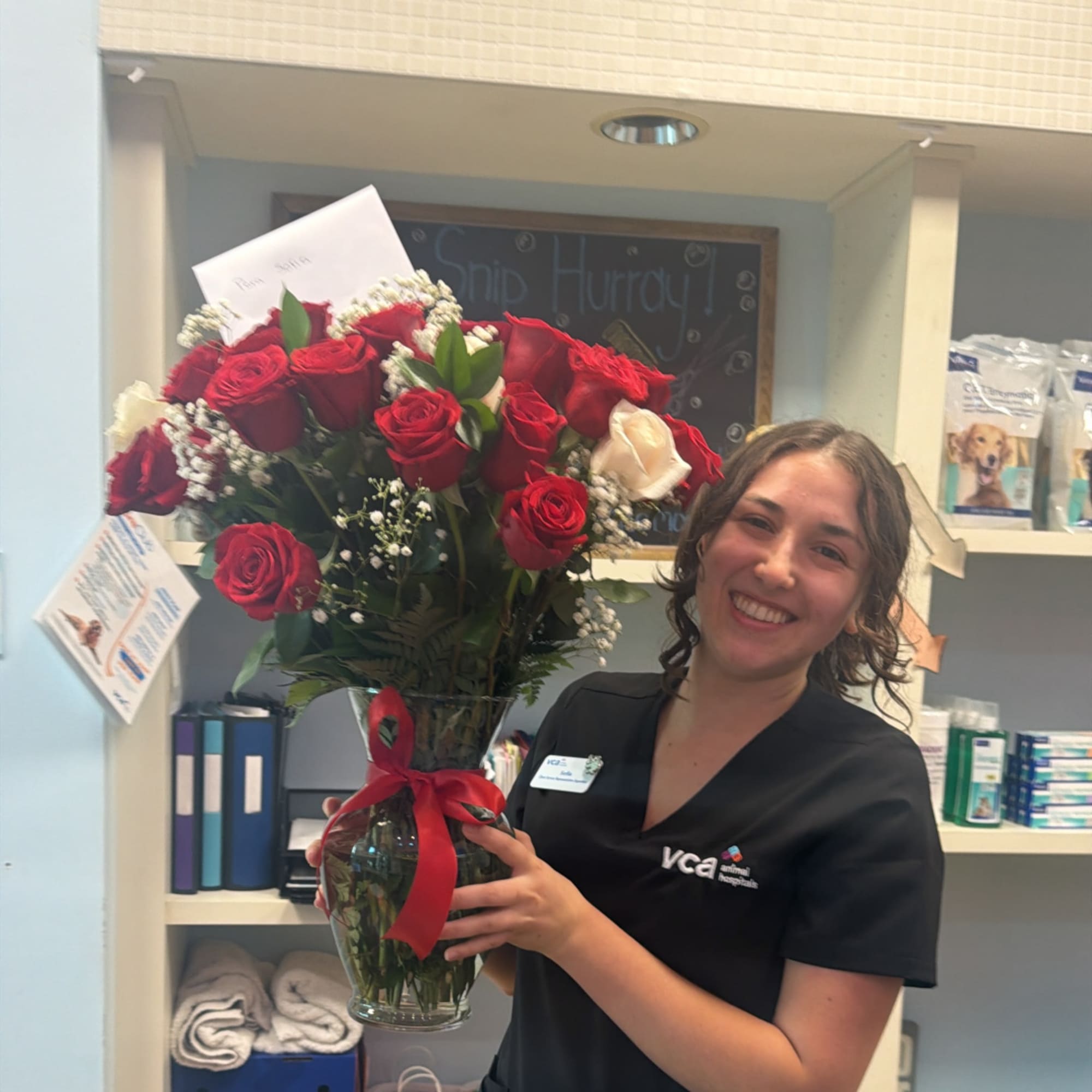 Woman holding a vase of red roses with a red ribbon