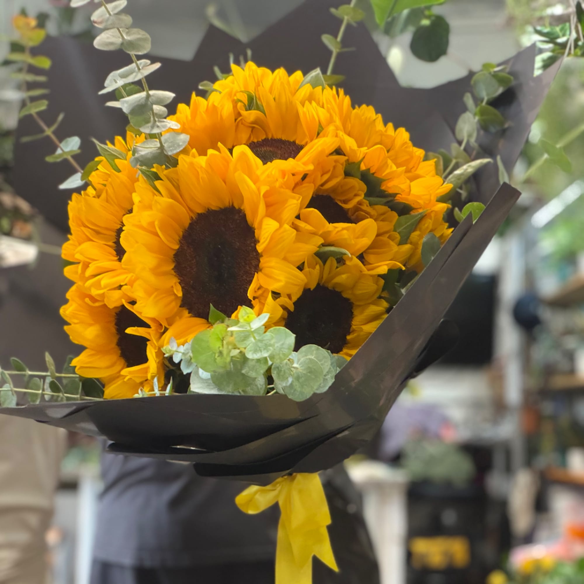Bouquet of yellow sunflowers wrapped in black paper with a yellow ribbon
