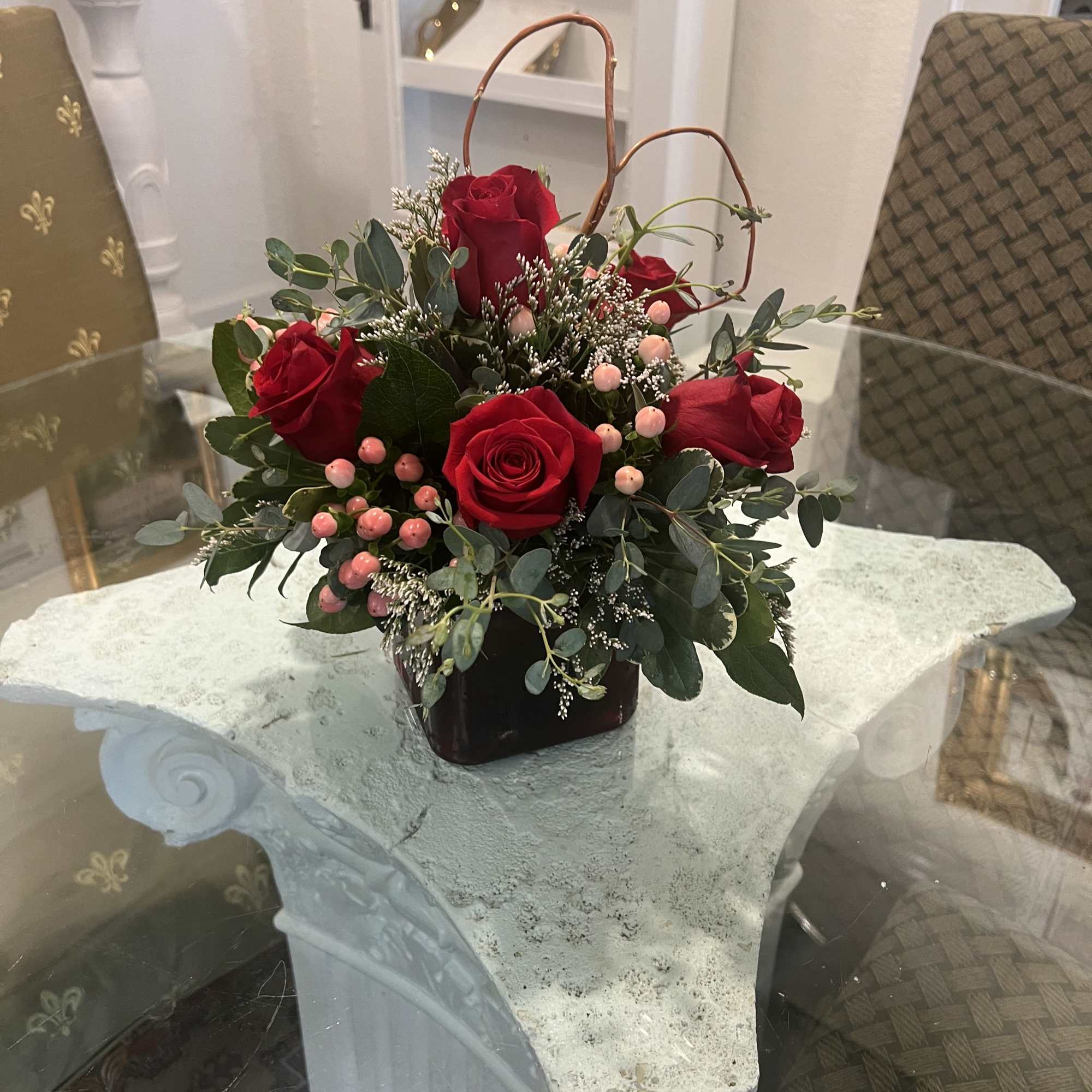 Red roses arranged in a dark vase with pink berries and greenery