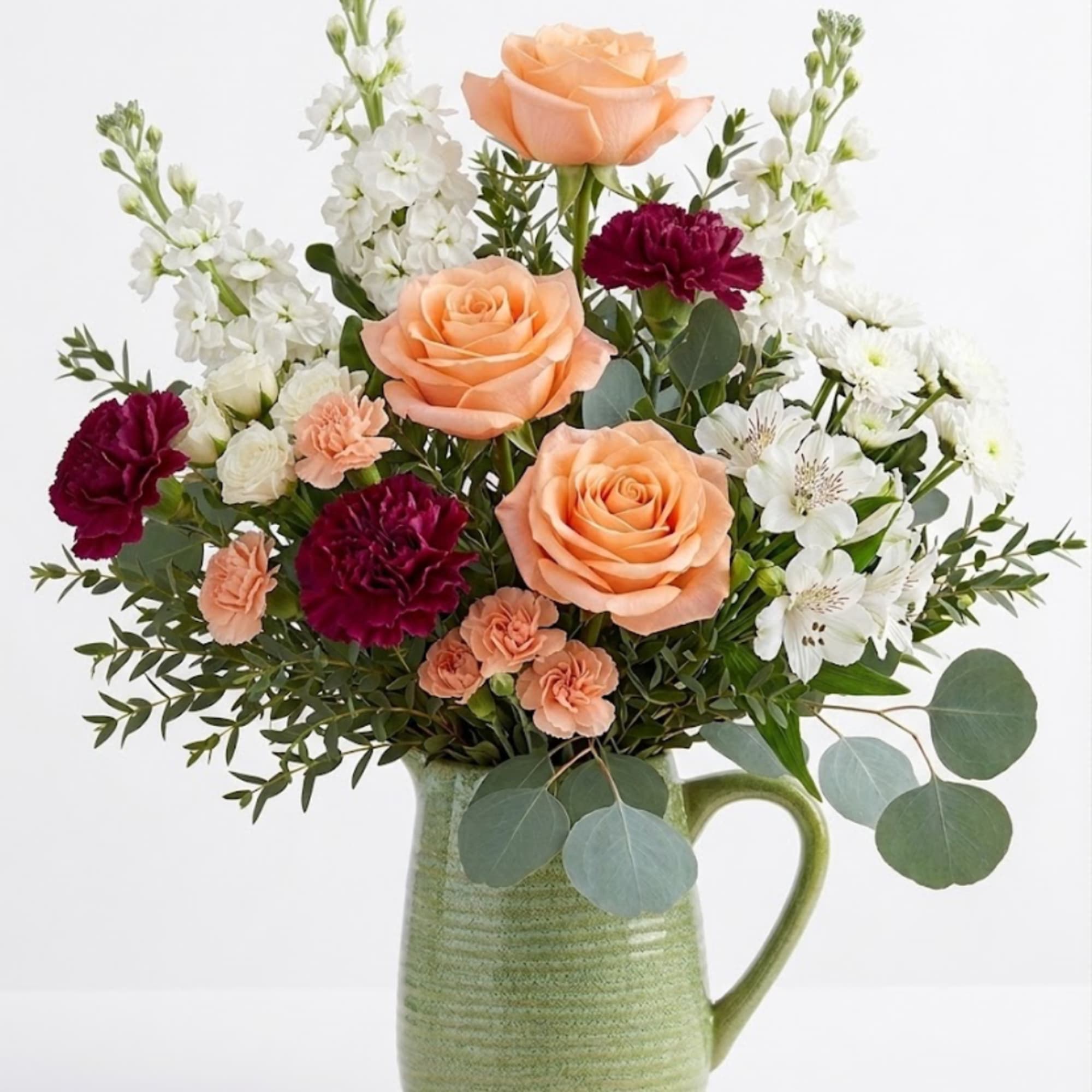 Peach roses and burgundy carnations in a green ceramic pitcher
