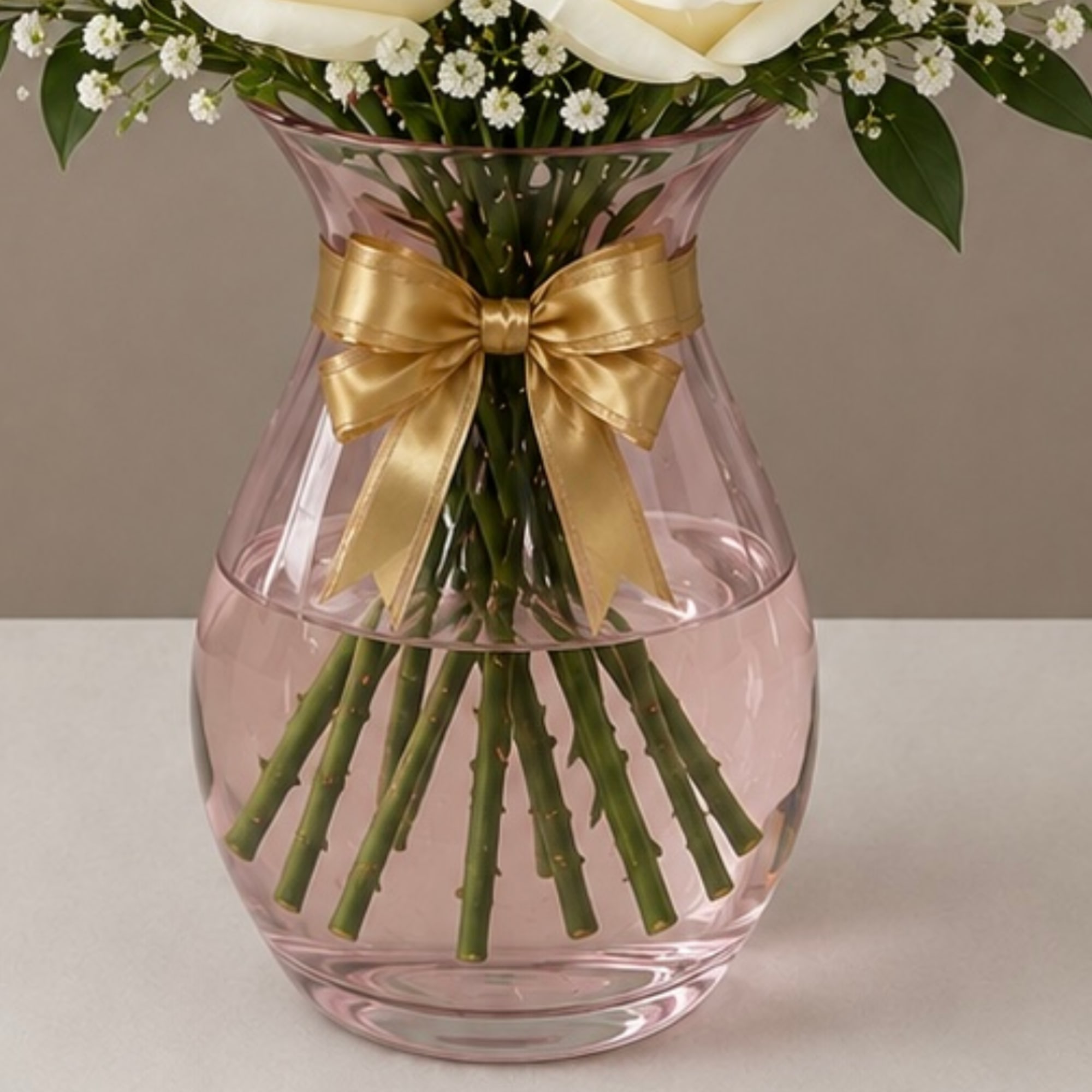 White flowers in a pink glass vase tied with a gold ribbon