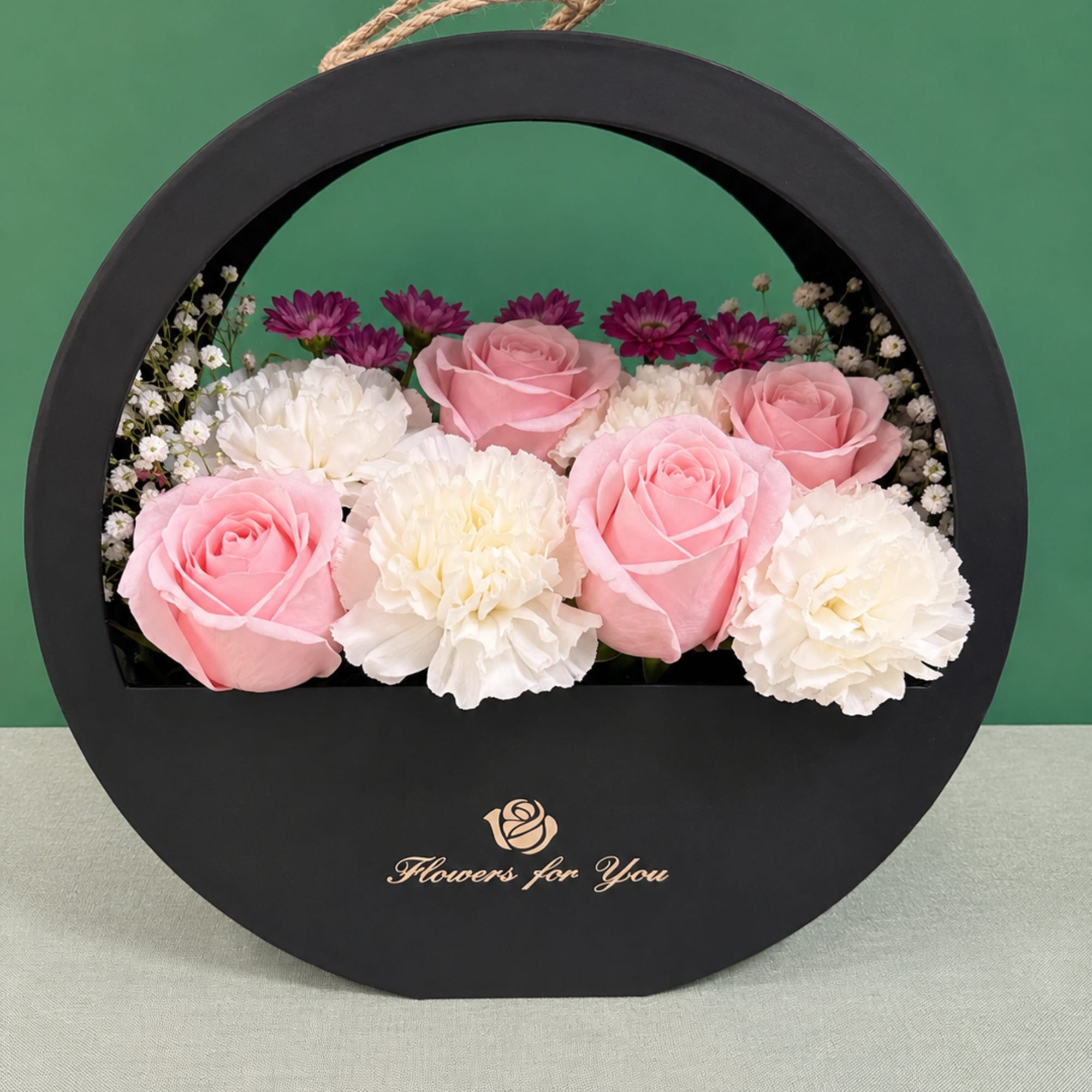 Pink roses and white carnations arranged in a round black gift box
