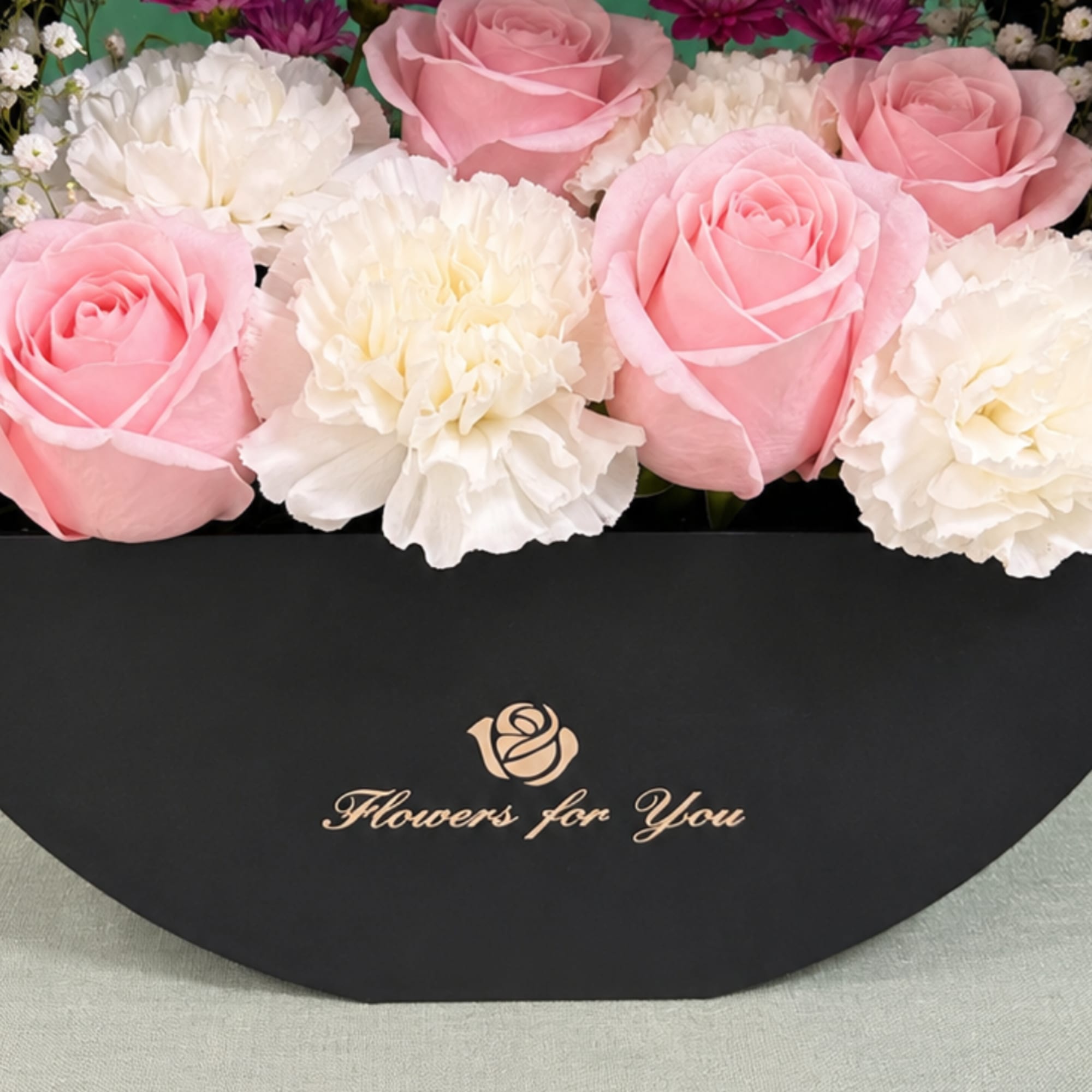 Pink roses and white carnations in a black round box