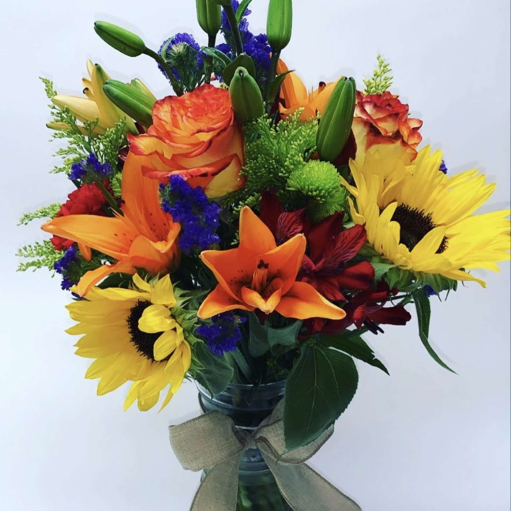 Colorful bouquet with sunflowers, lilies, and roses in a glass vase