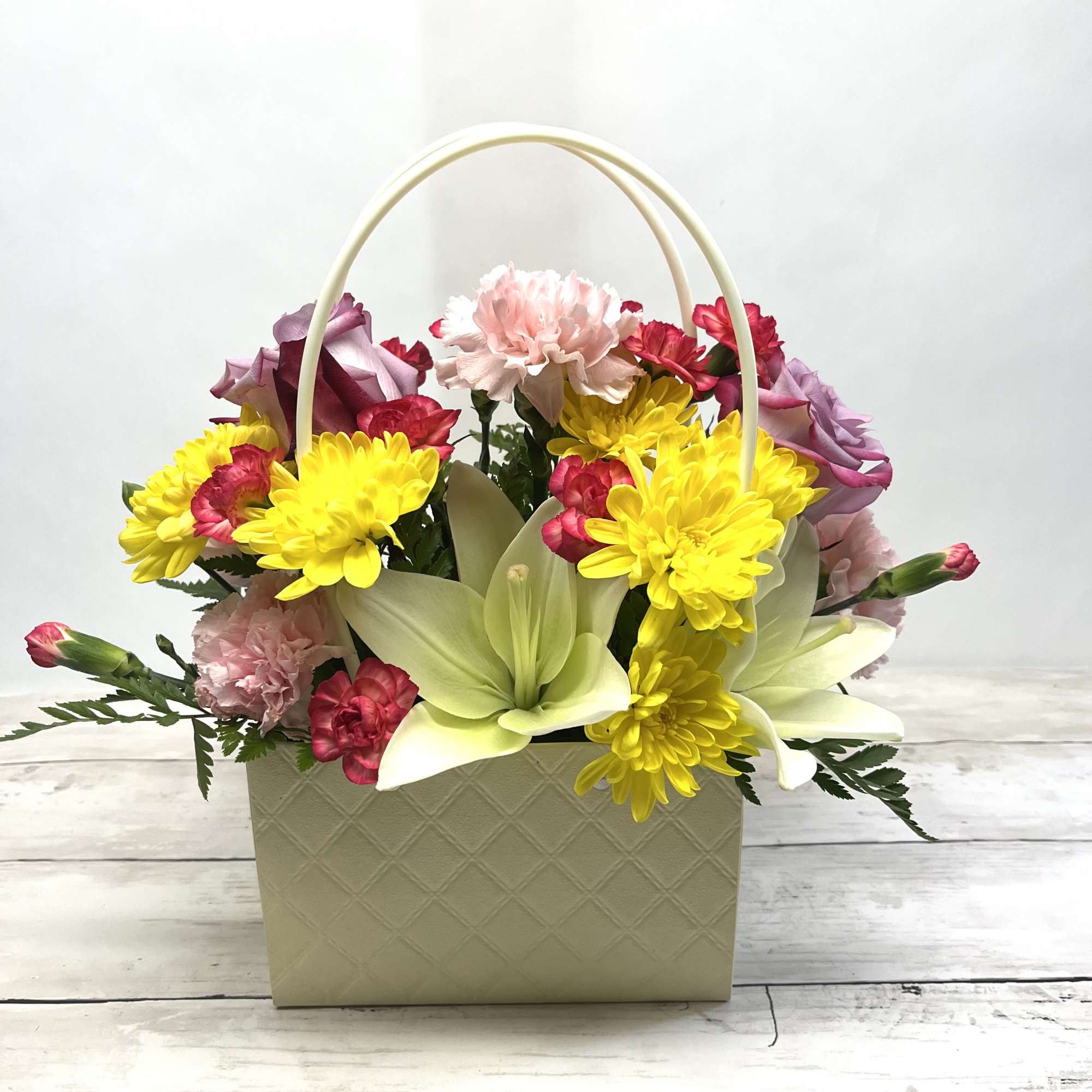 Basket arrangement with yellow daisies, pink carnations, and pale lilies
