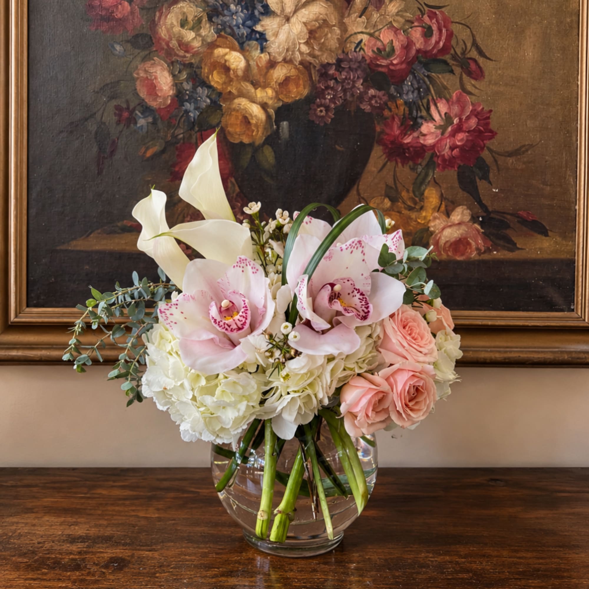 Pink orchids and roses in a clear glass vase with white hydrangeas