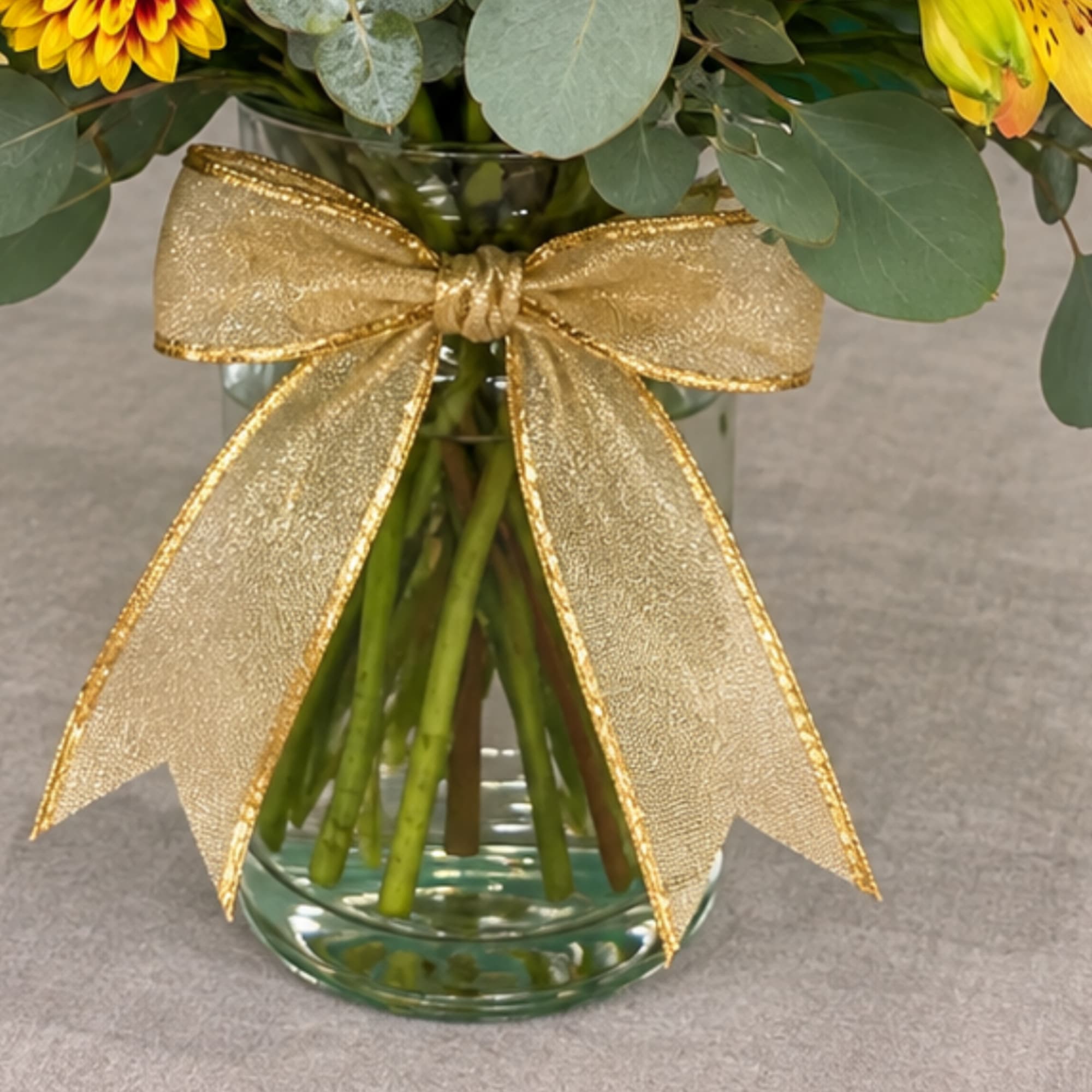 Yellow flowers in a glass vase tied with a gold ribbon