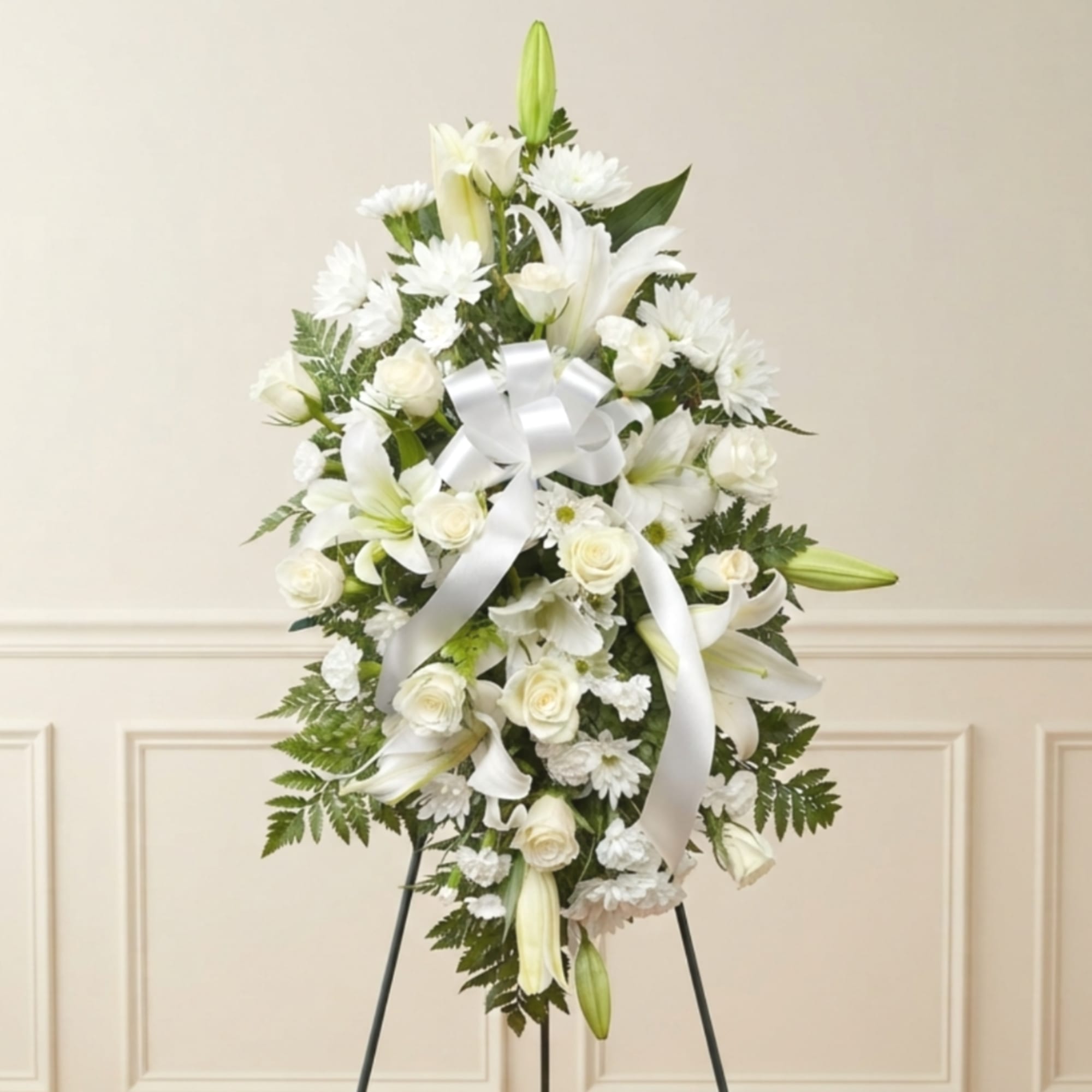 White floral standing spray with lilies, roses, and daisies on an easel