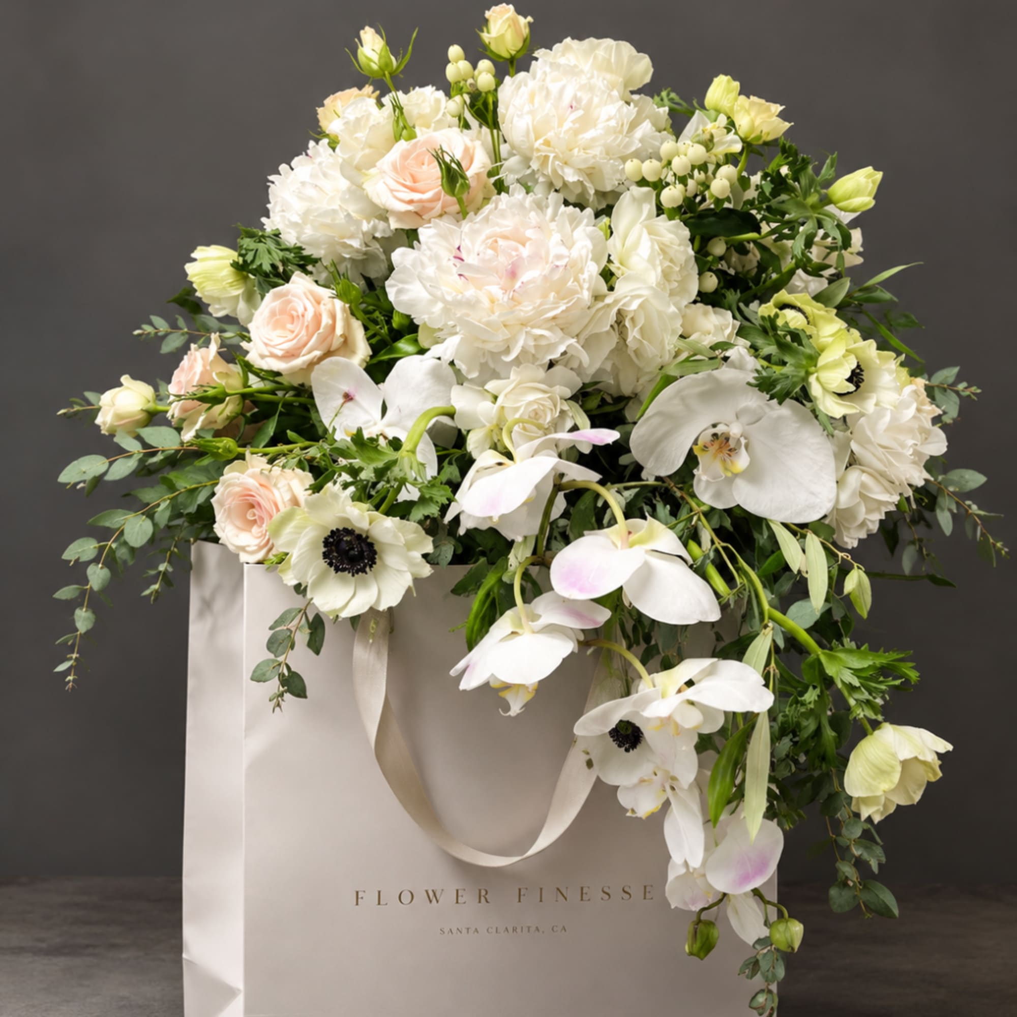 White and blush floral arrangement in a gift bag with trailing greenery