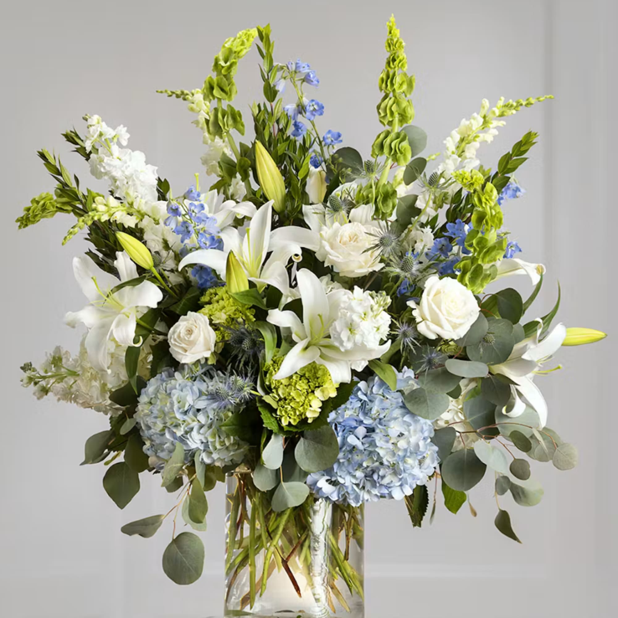 White lilies and roses with blue hydrangeas in a glass vase