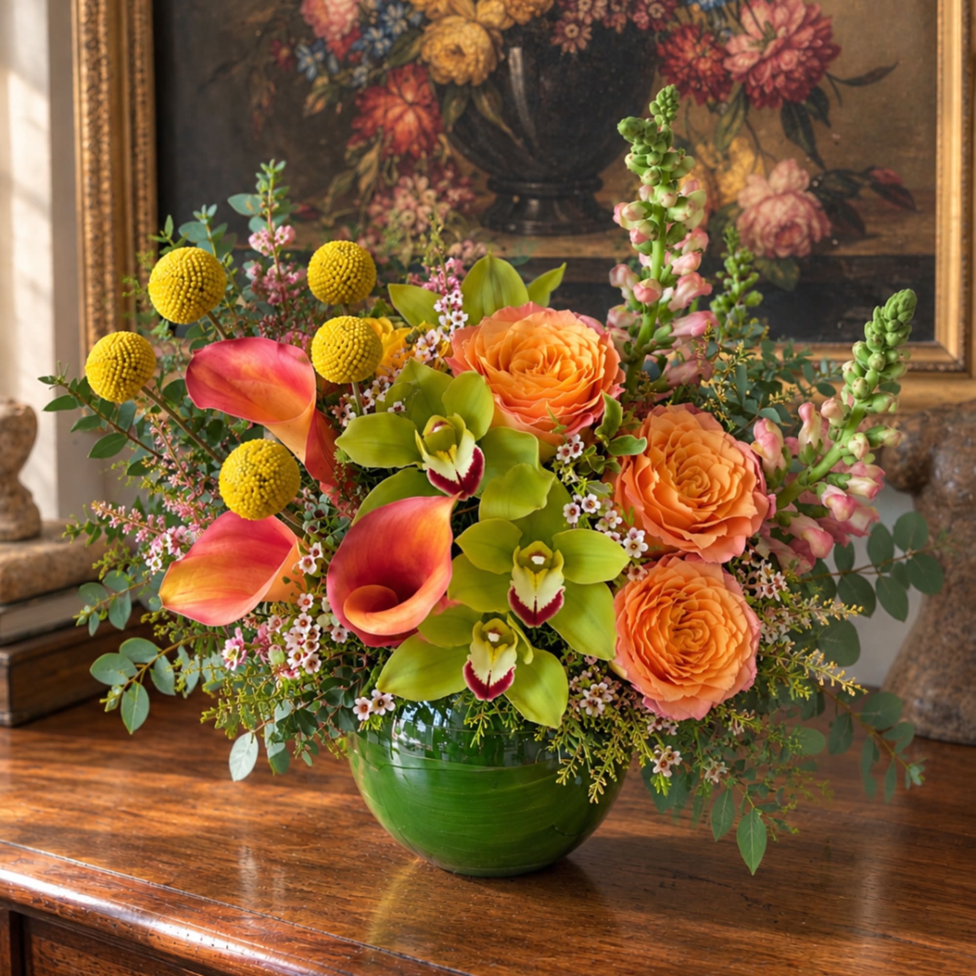 Orange roses, calla lilies, and yellow pom flowers in a green vase