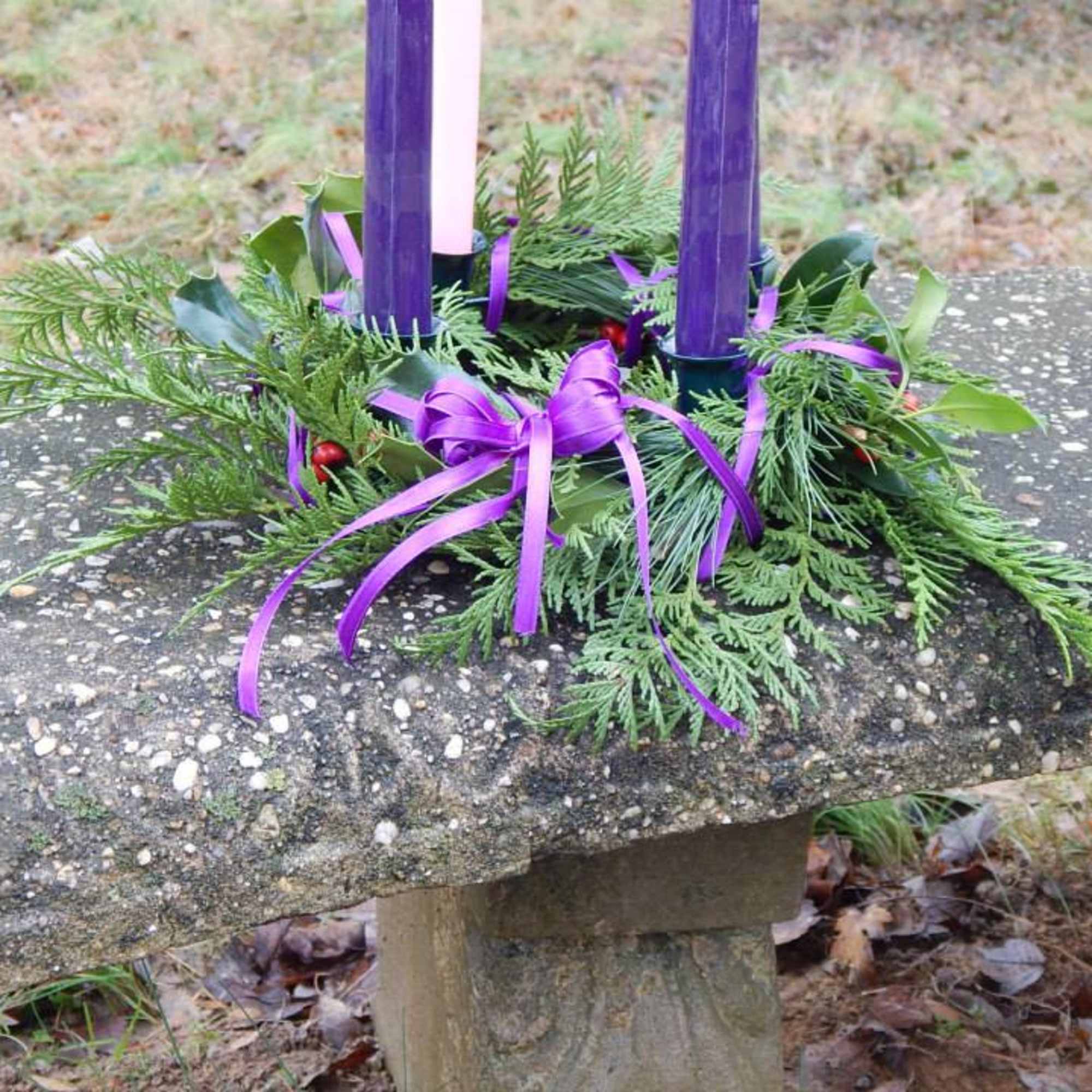 Purple candles in a greenery wreath with ribbon on a stone bench