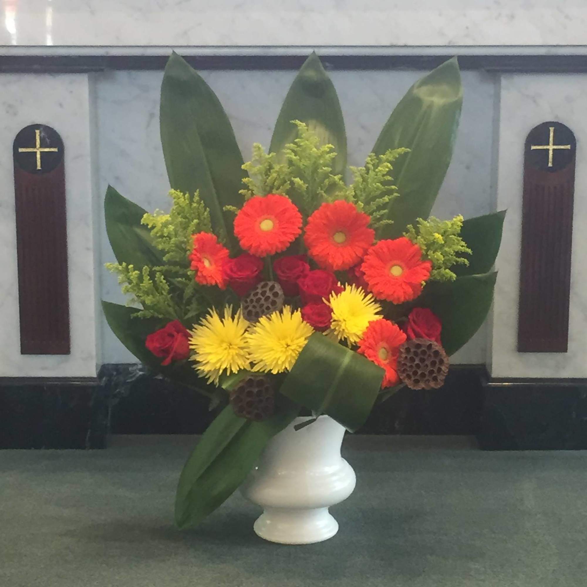 Colorful floral arrangement in a white vase with red, yellow, and orange blooms