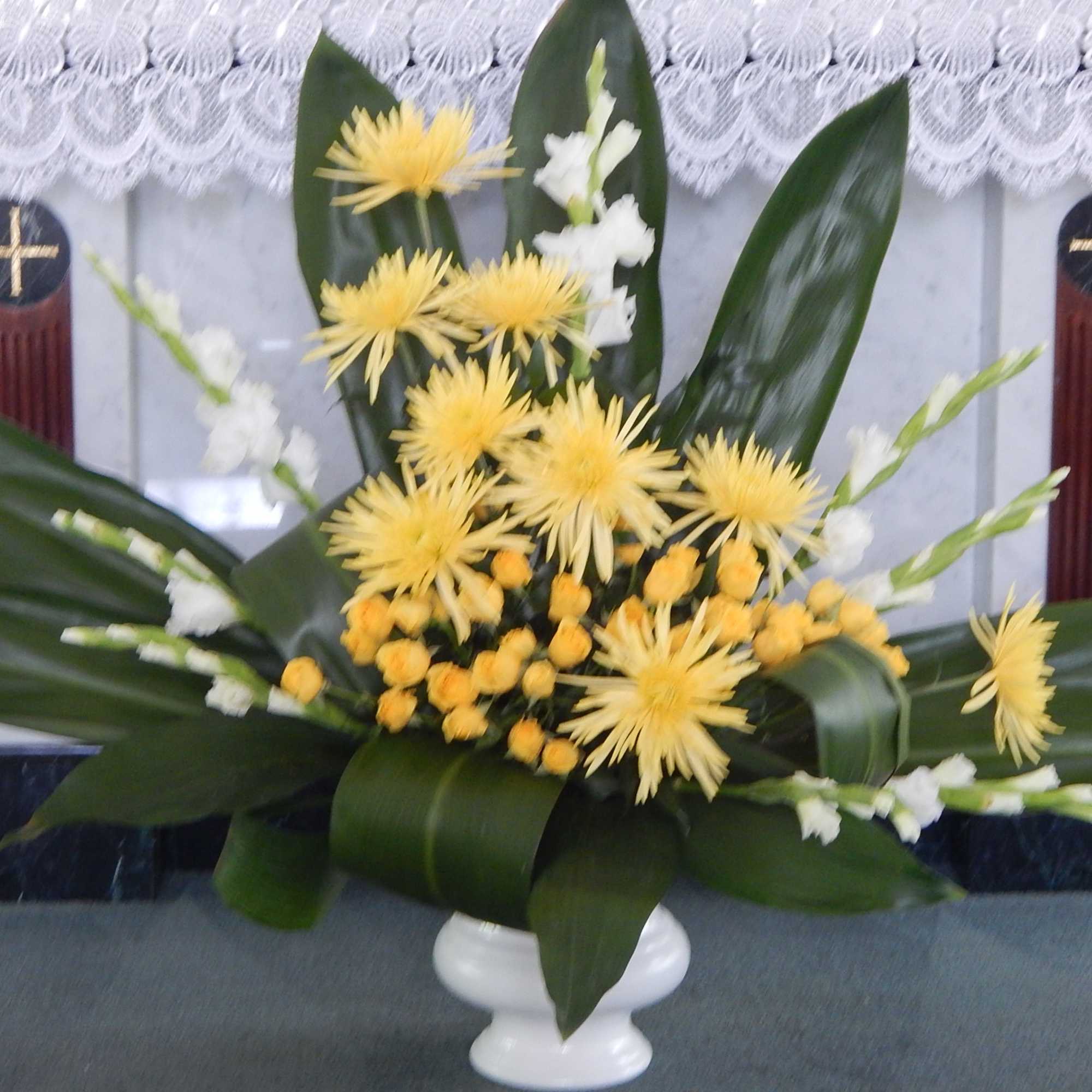 Yellow and white floral arrangement in a white pedestal vase
