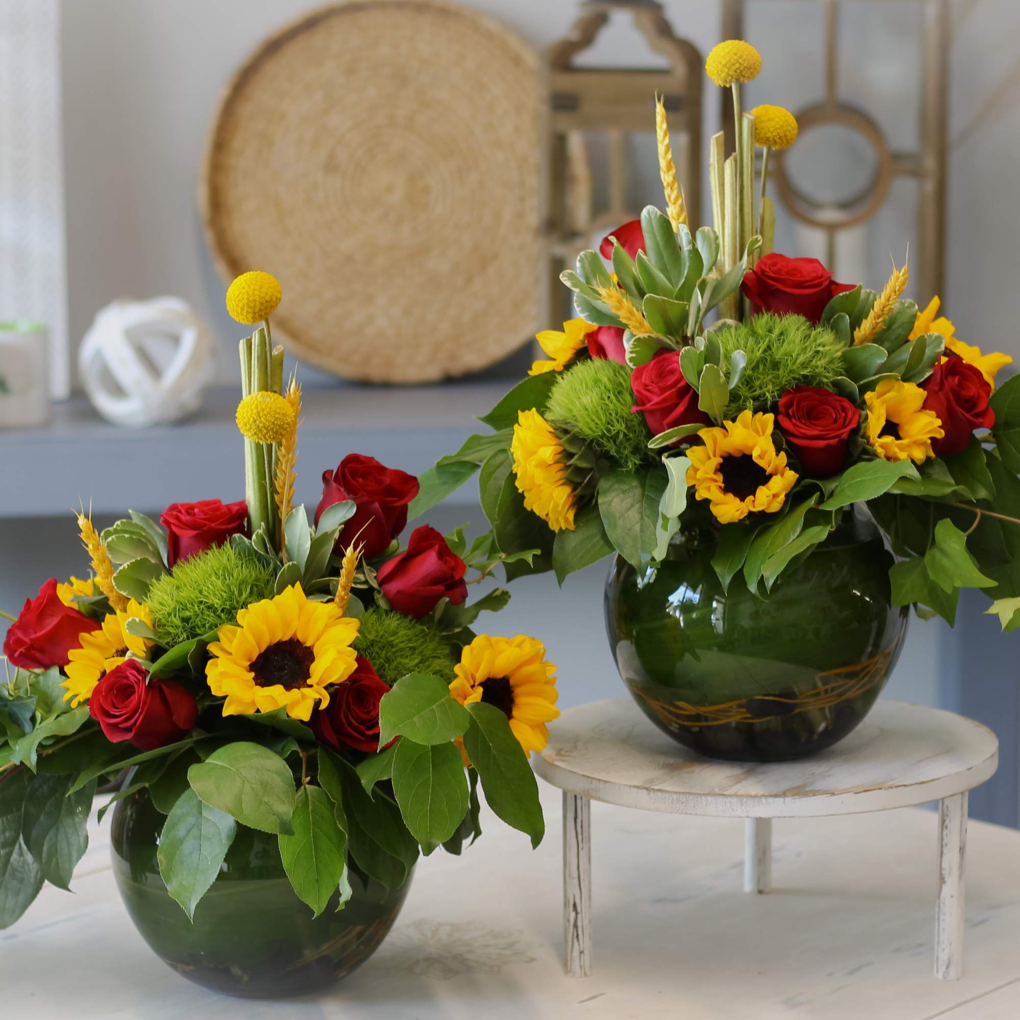 Two floral arrangements with red roses and yellow sunflowers in dark glass vases.