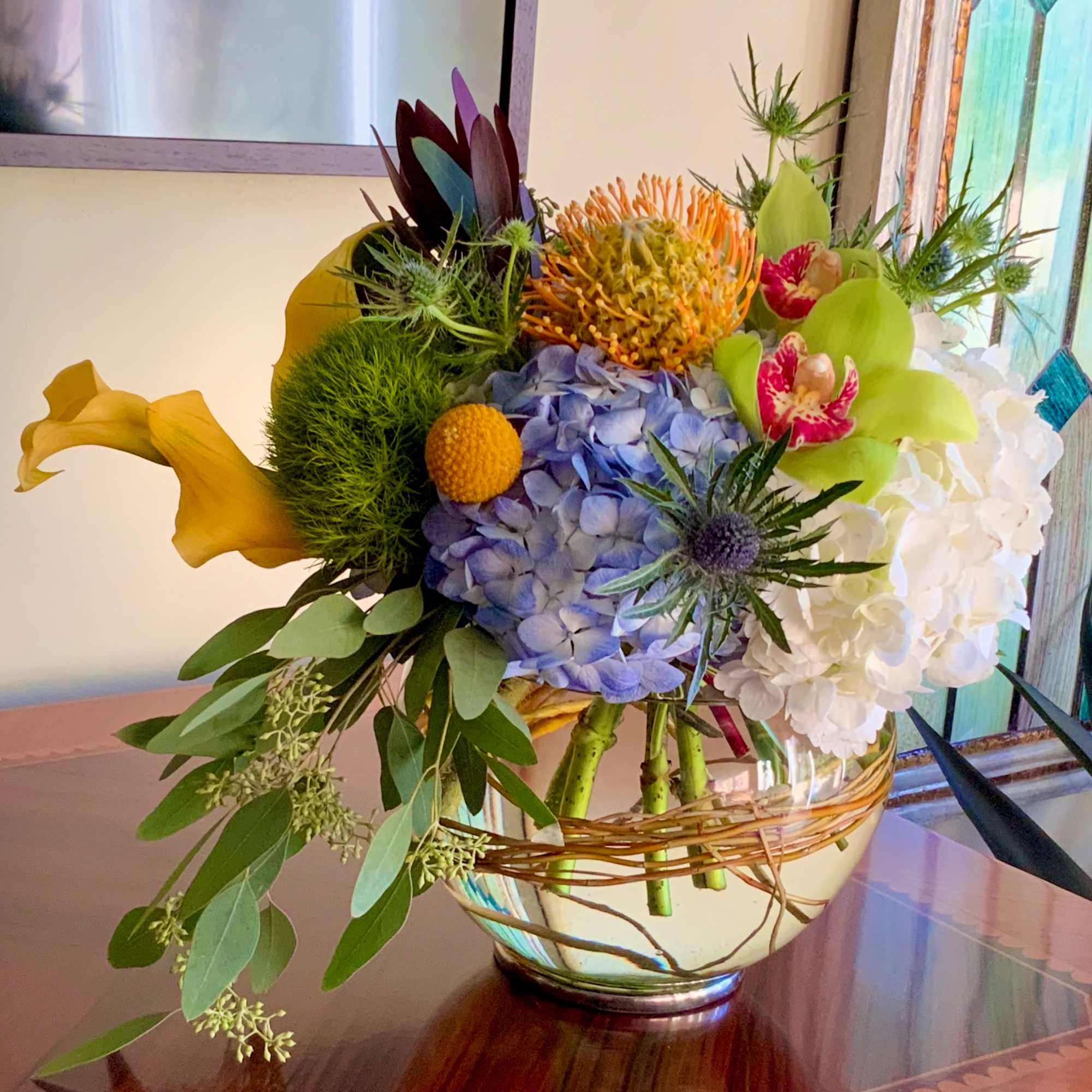 Mixed bouquet in a glass bowl with blue hydrangea, white blooms, and yellow calla lilies