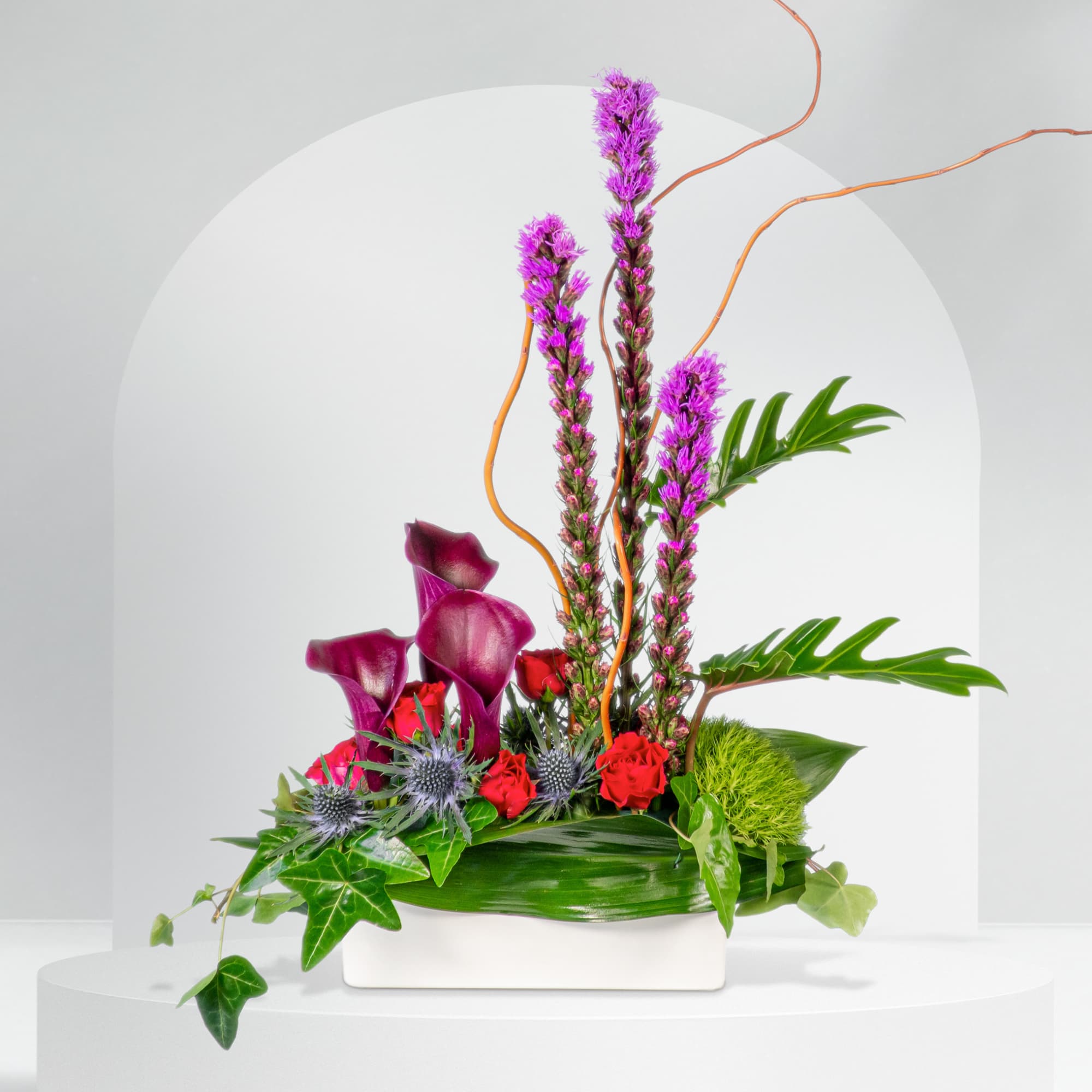Arrangement of purple calla lilies and red roses in a white container