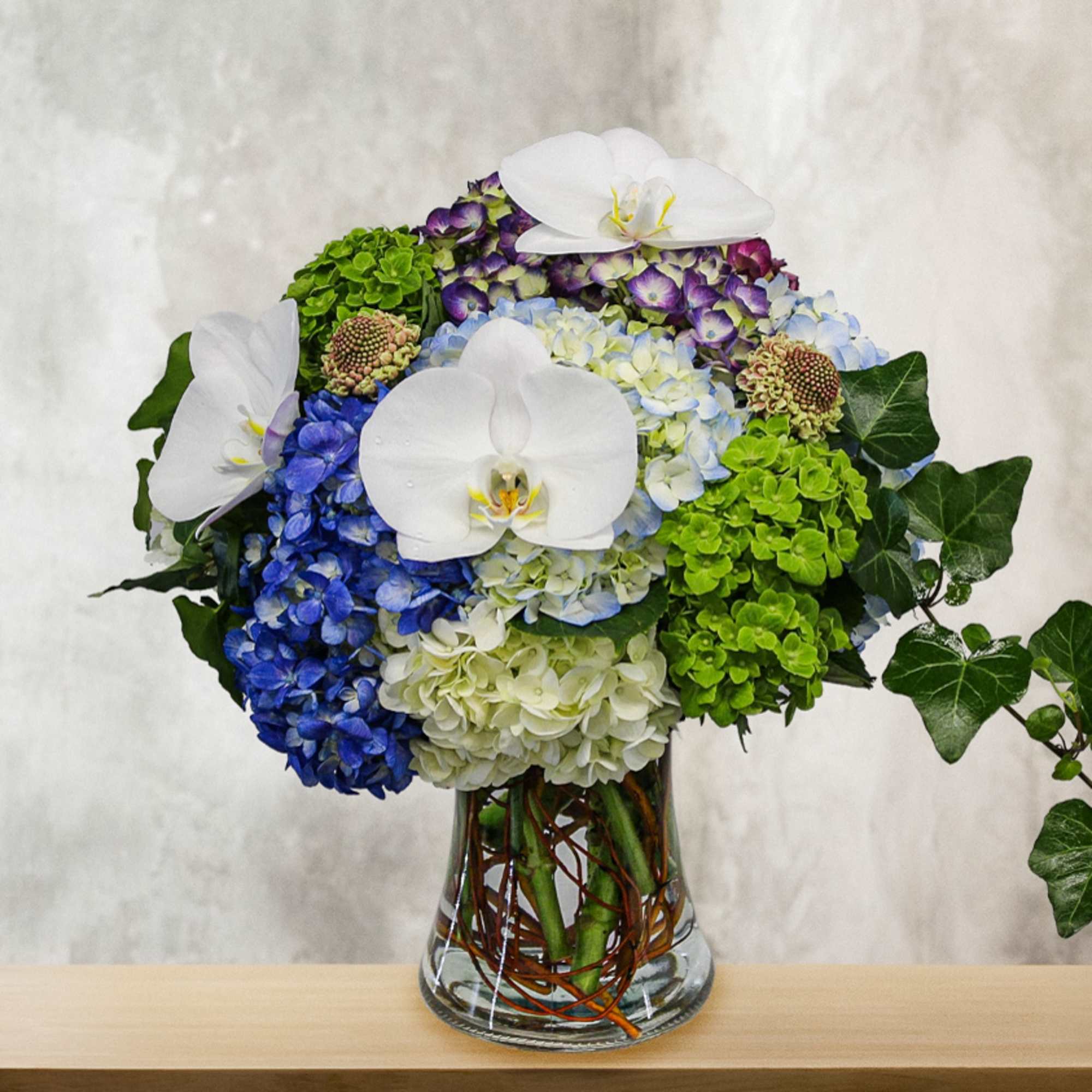 Blue and green hydrangea arrangement with white orchids in a glass vase, photo 2 of 2