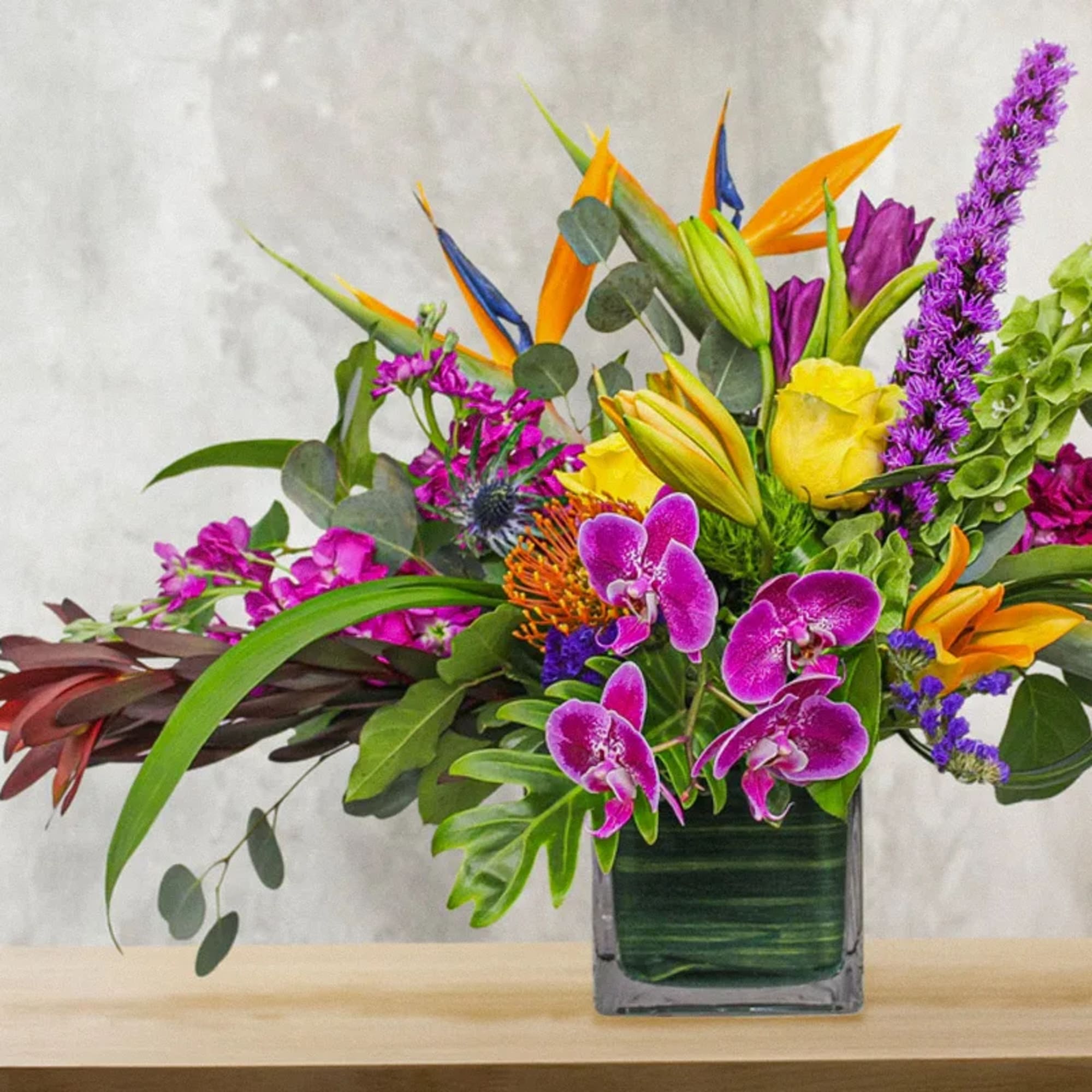 Tropical bouquet with purple orchids and orange bird-of-paradise in a square vase