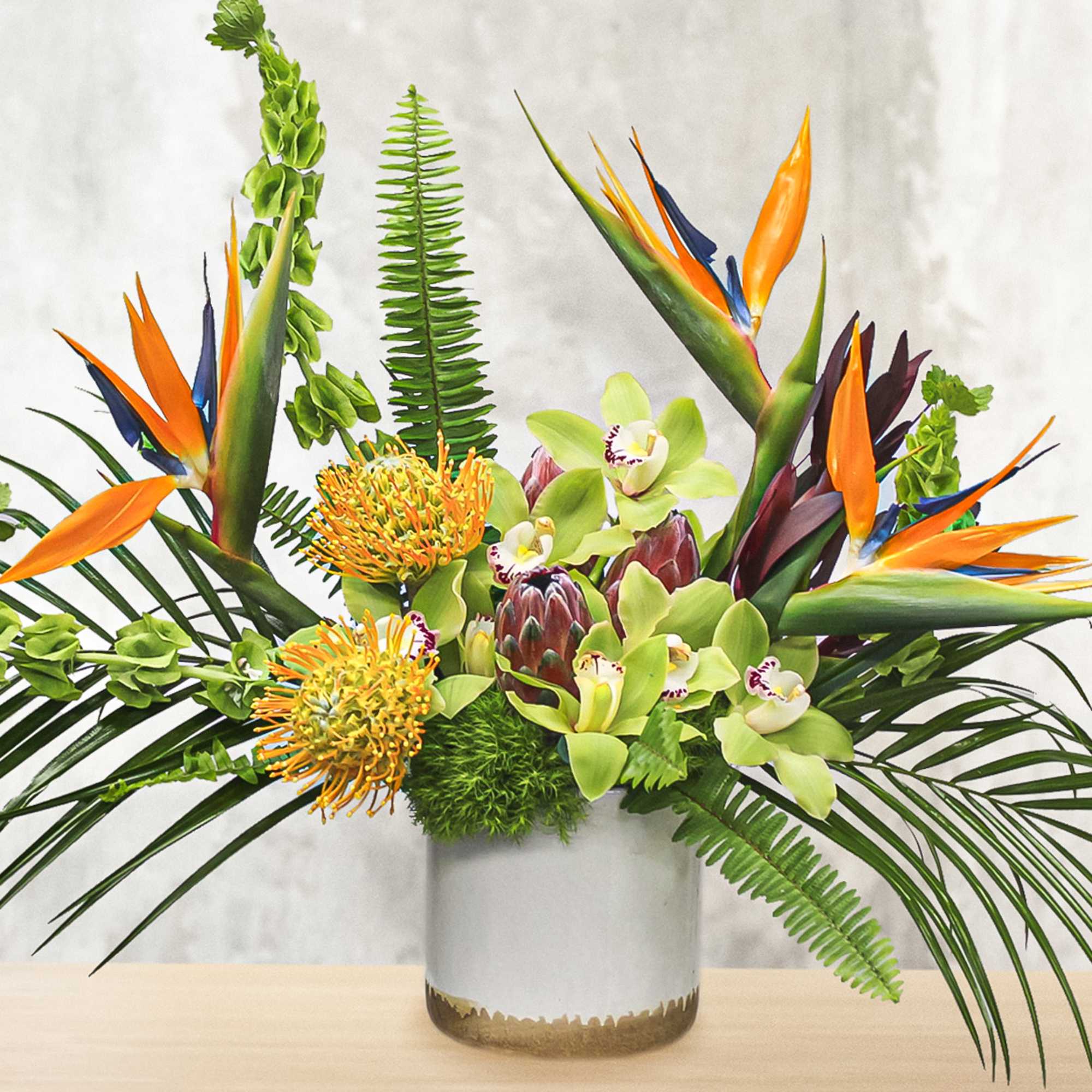Tropical flower arrangement in a glass vase with orange bird-of-paradise and green orchids