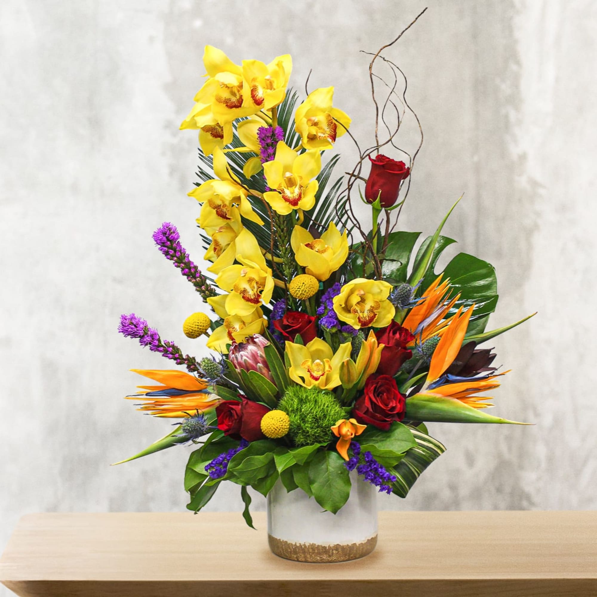 Tall tropical bouquet with yellow orchids, red roses, and orange bird-of-paradise in a vase