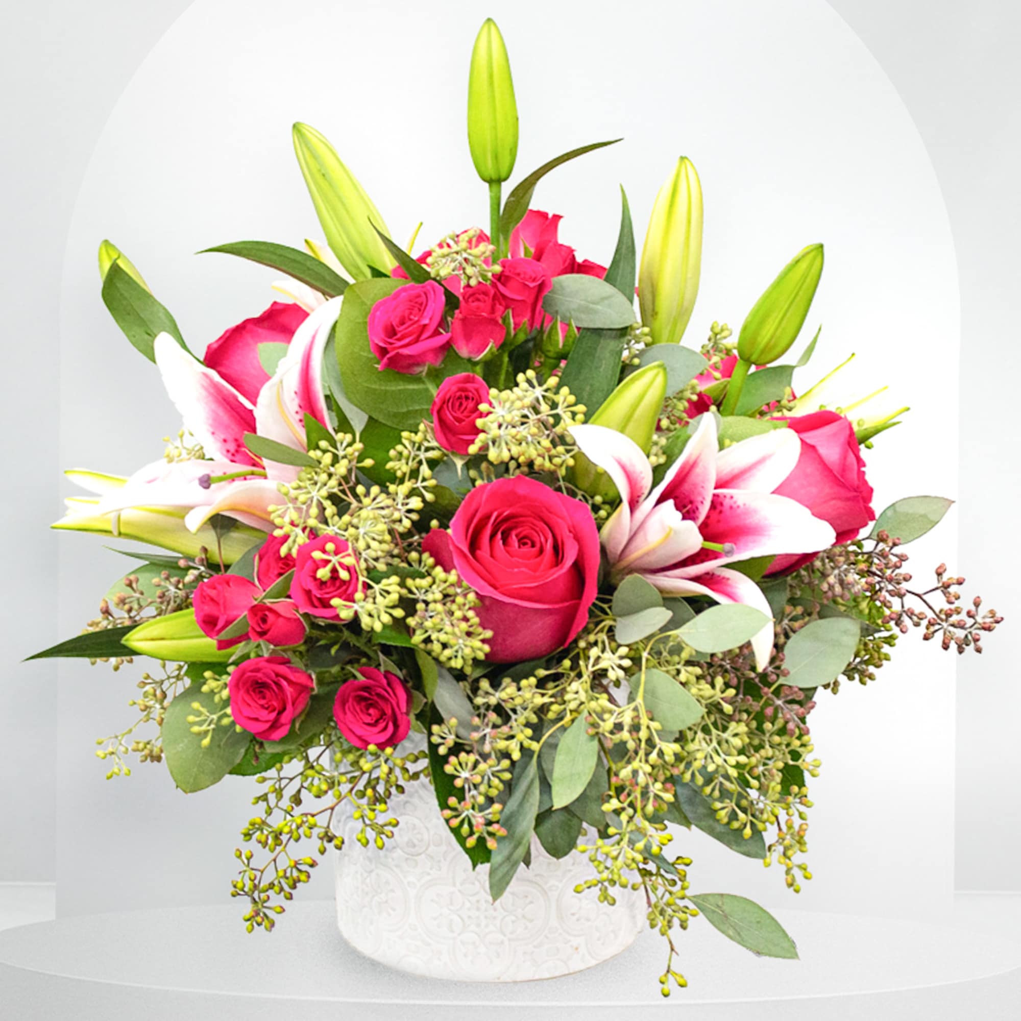 Pink roses and white lilies arranged in a white vase