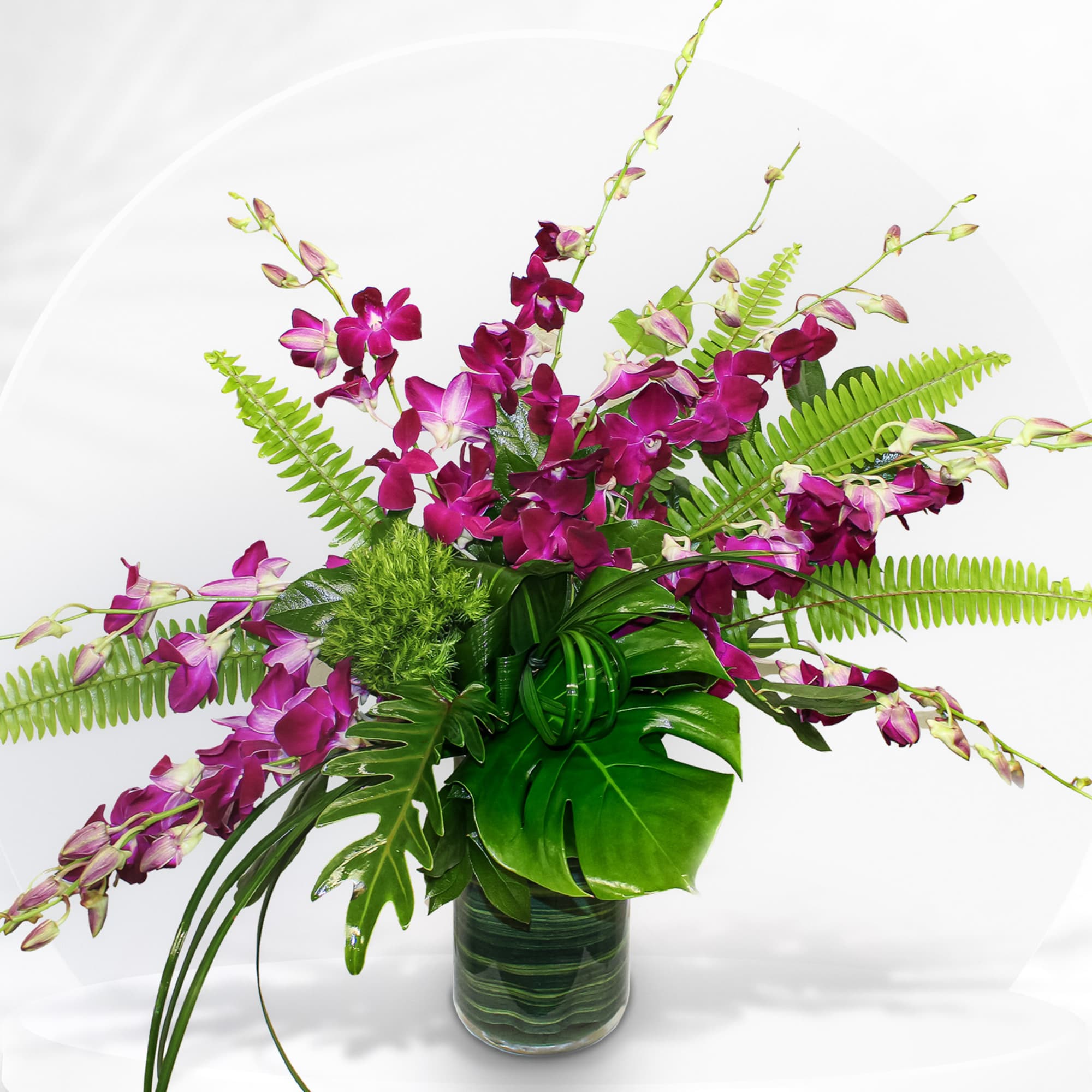 Purple orchid arrangement in a glass vase with tropical foliage
