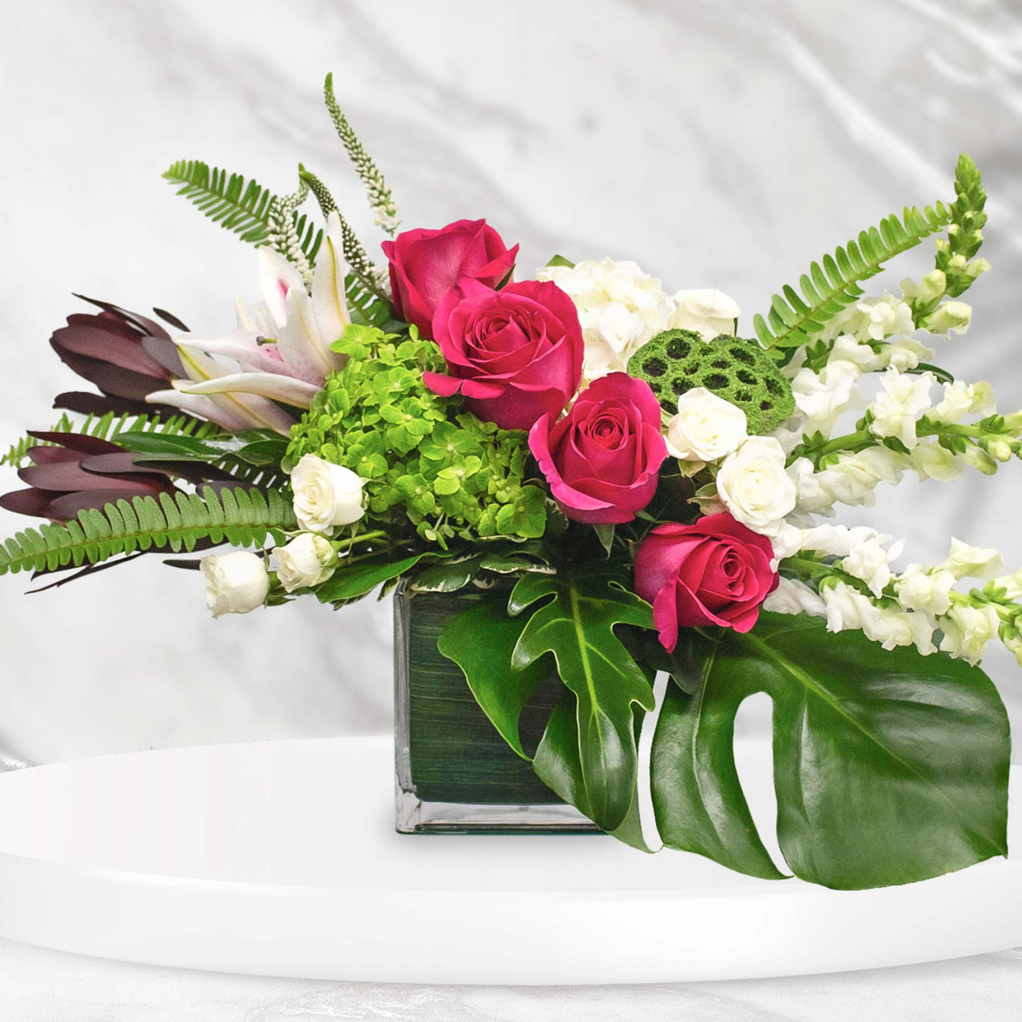 Pink roses and white flowers in a glass vase with tropical leaves