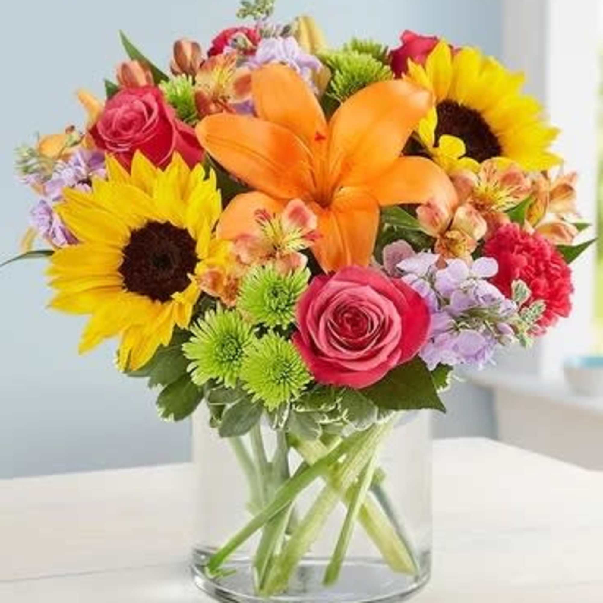 Colorful bouquet with sunflowers, roses, and lilies in a glass vase