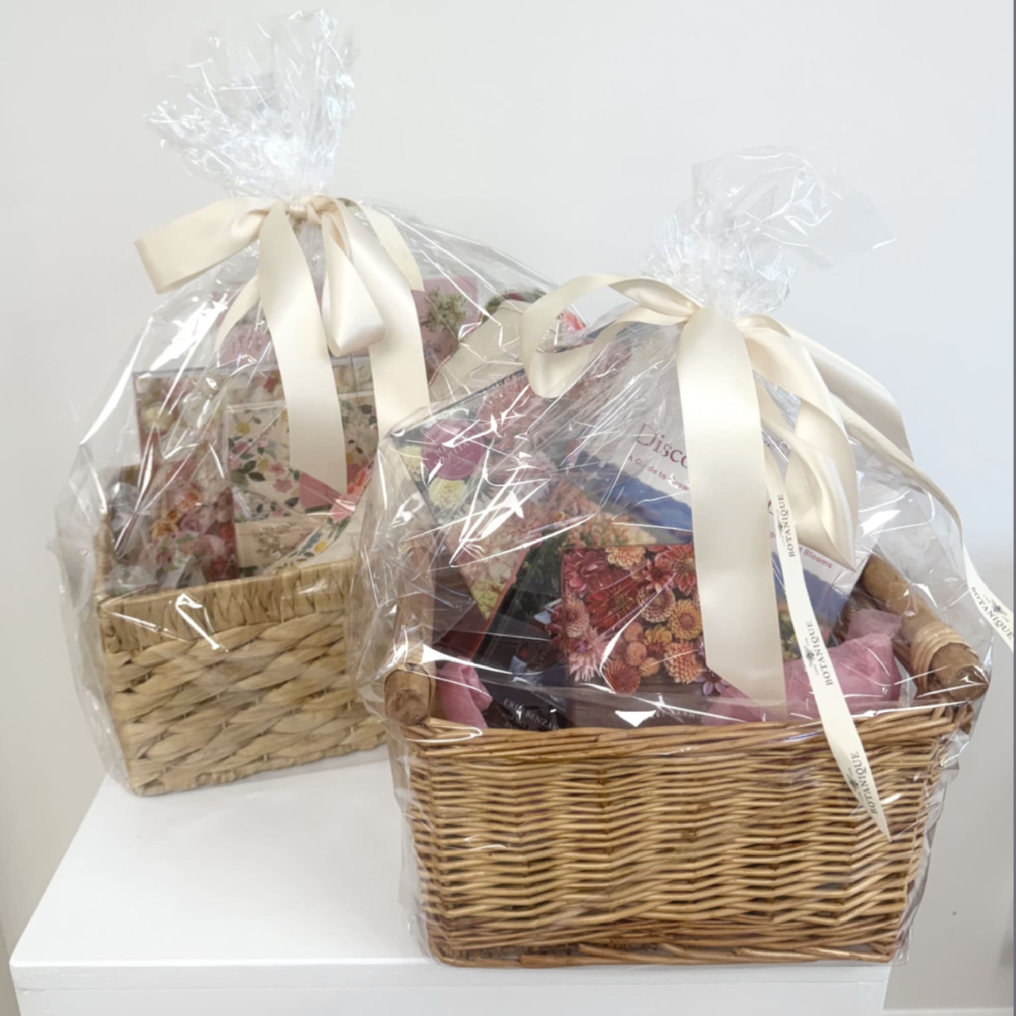 Two wicker gift baskets wrapped in clear cellophane with cream ribbons