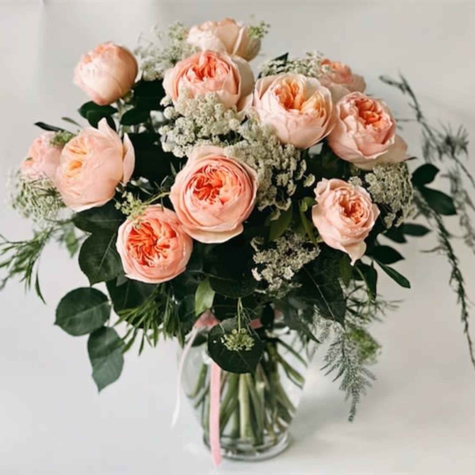 Peach garden roses and white filler flowers arranged in a clear glass vase