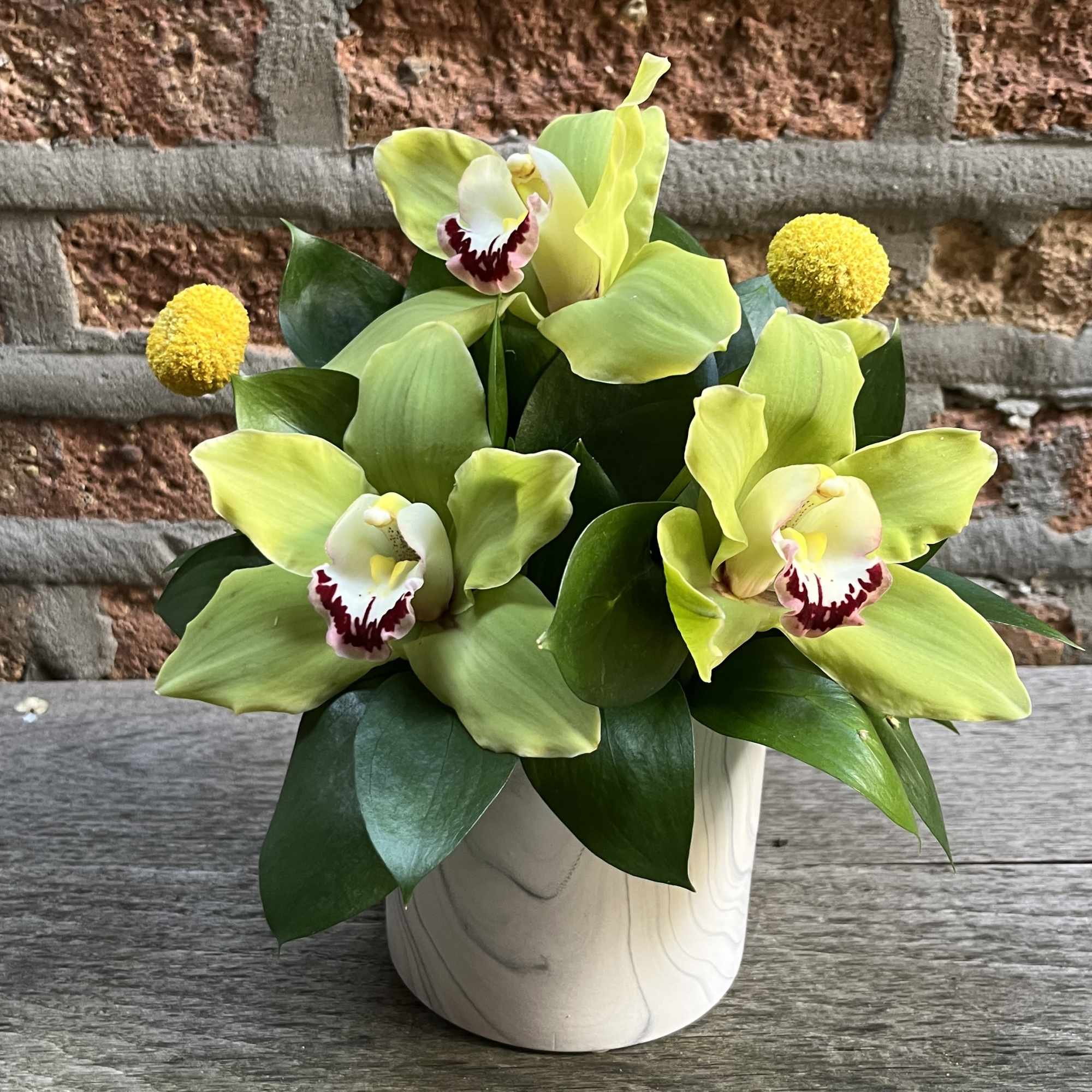 Green orchid arrangement in a white vase with yellow accents