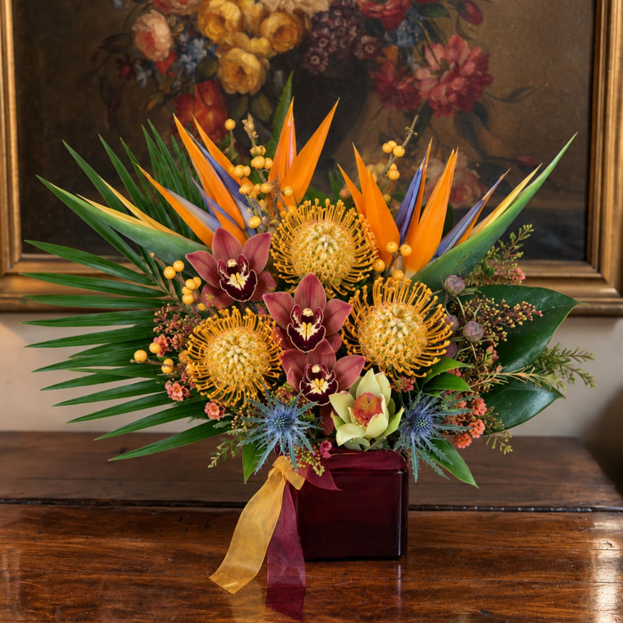 Tropical flower arrangement in a burgundy vase with orange and purple blooms