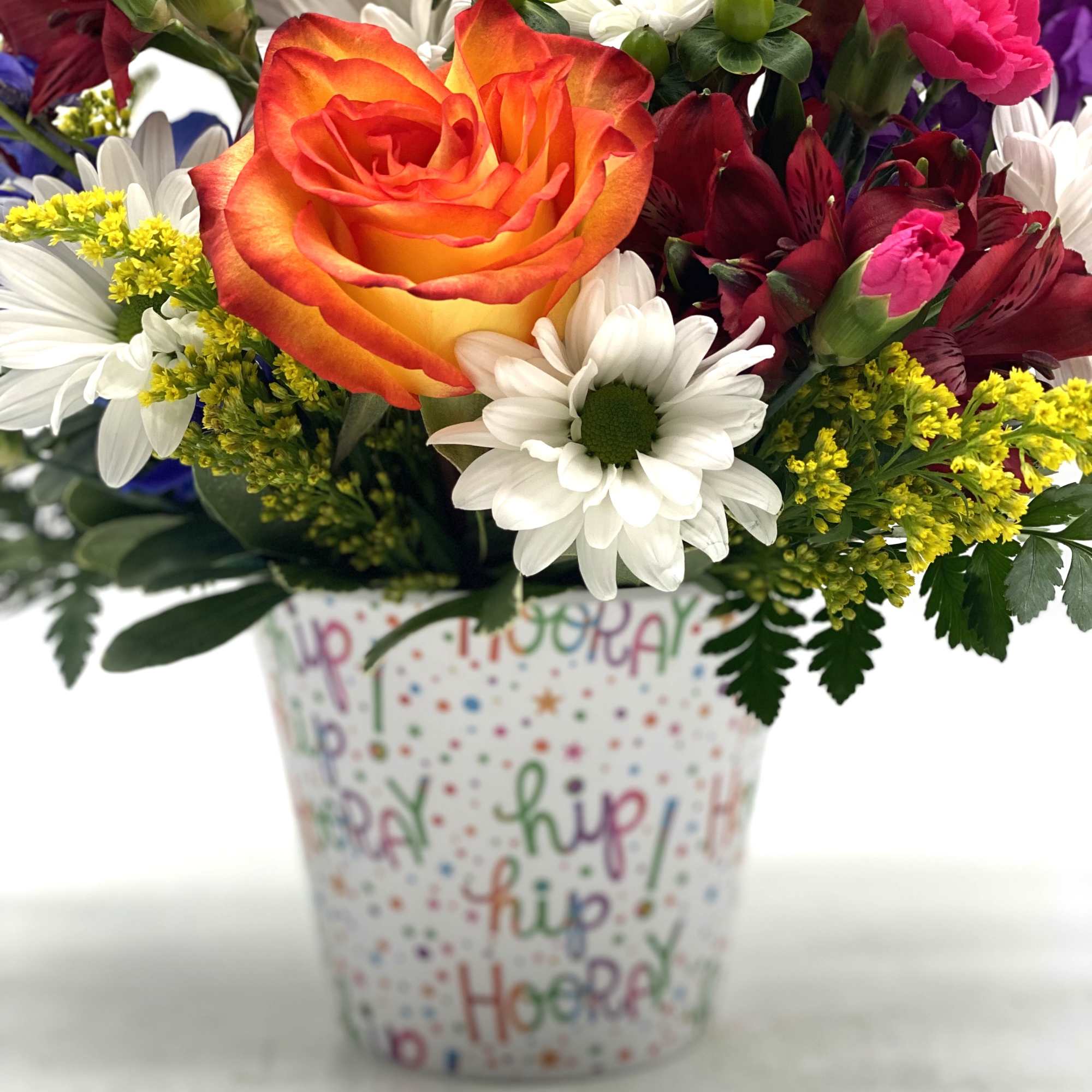 Mixed bouquet in a decorated cup with an orange rose and white daisies