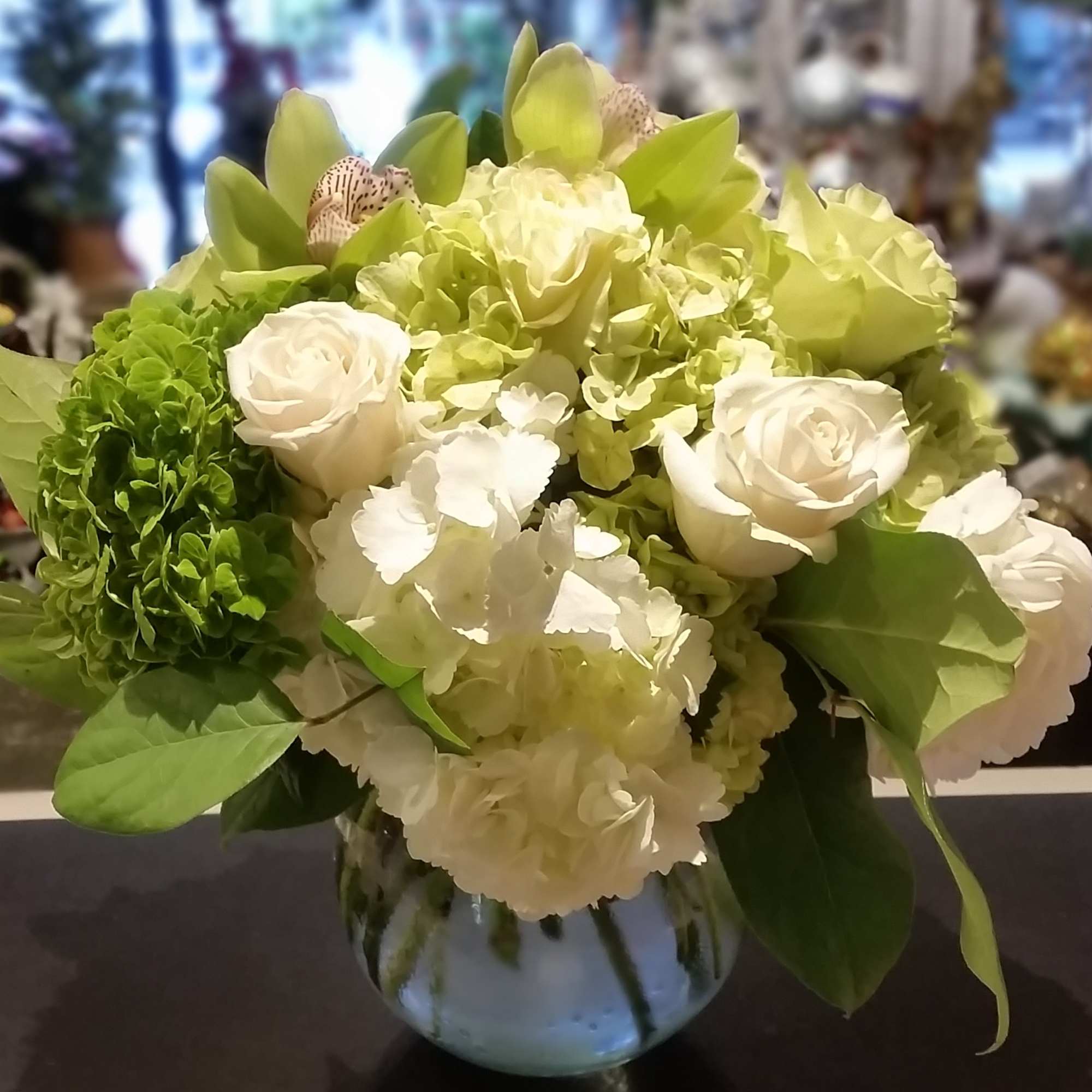 White and green roses, hydrangeas, and orchids arranged in a round clear glass vase