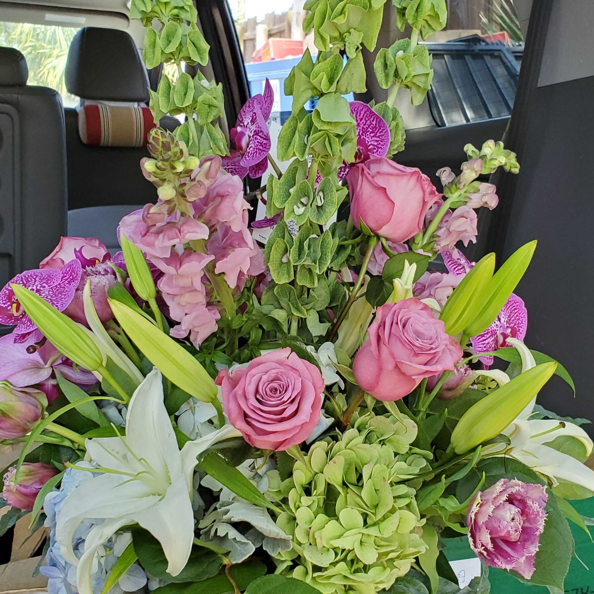 Tall arrangement of pink roses, white lilies, orchids, and green hydrangeas in a clear glass vase