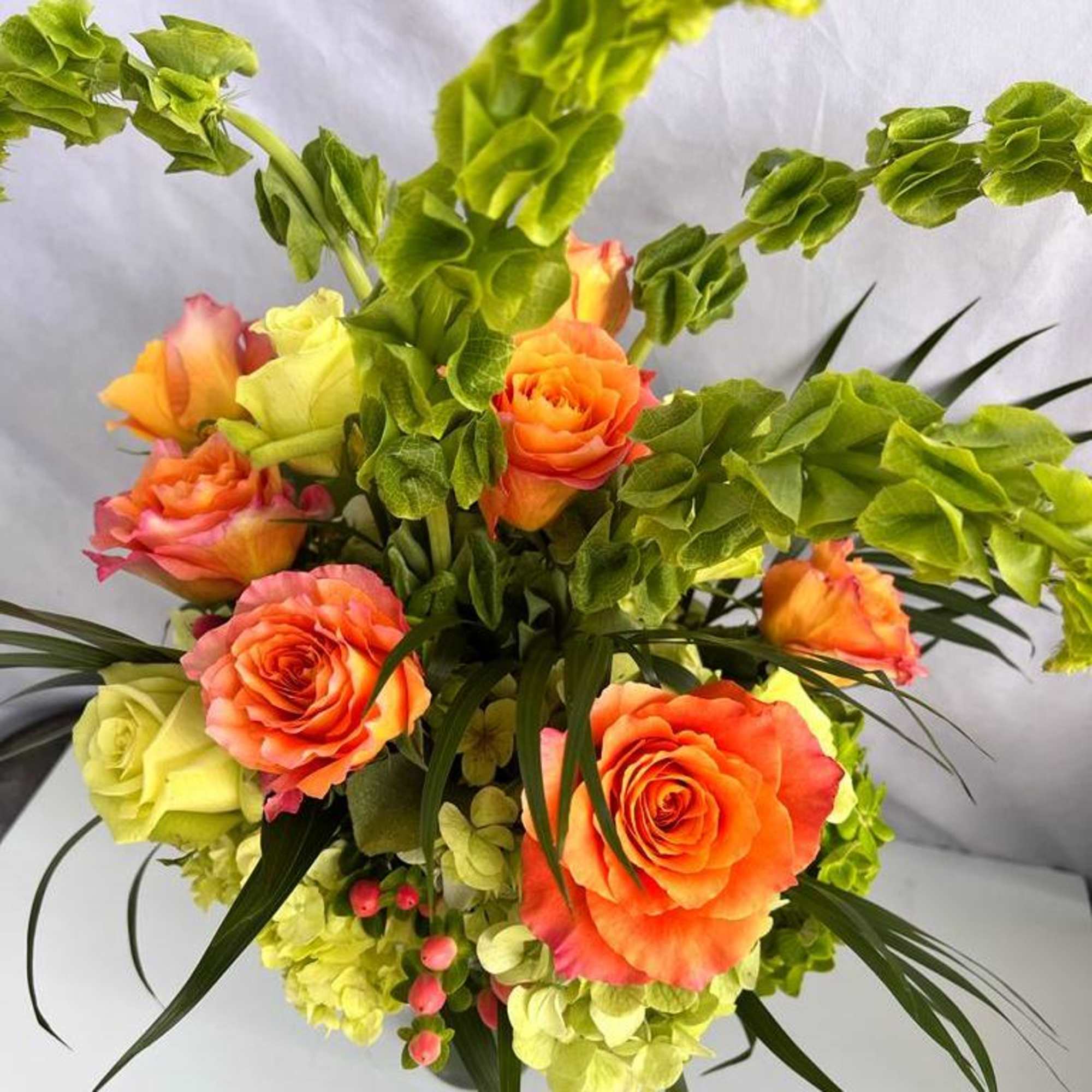 Arrangement of orange roses with green Bells of Ireland and hydrangeas in a compact display