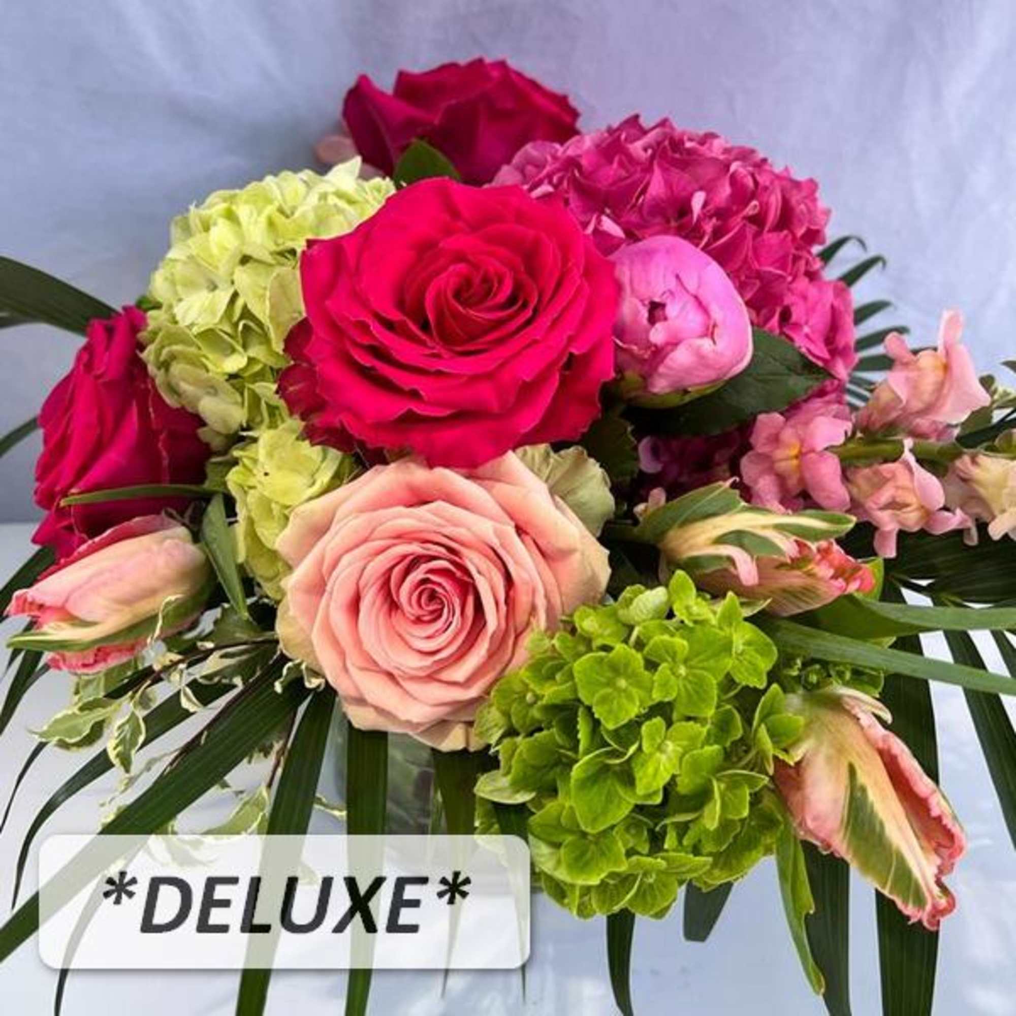 Low arrangement of hot pink and blush roses with green hydrangeas and pink blooms in a clear vase