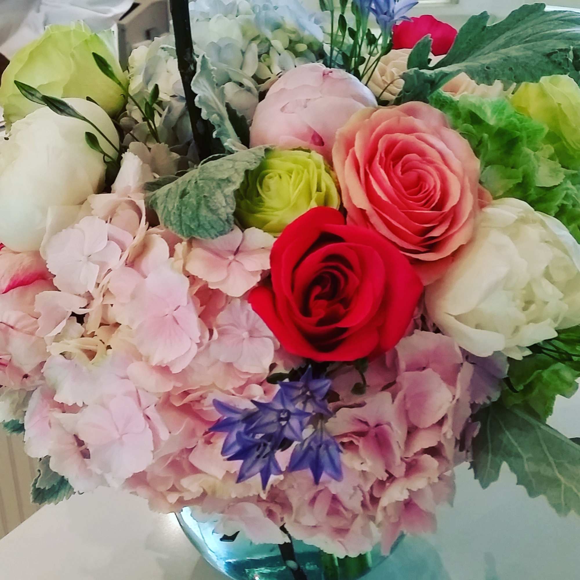 Round arrangement of pink hydrangeas with mixed roses and white blooms in a clear glass vase