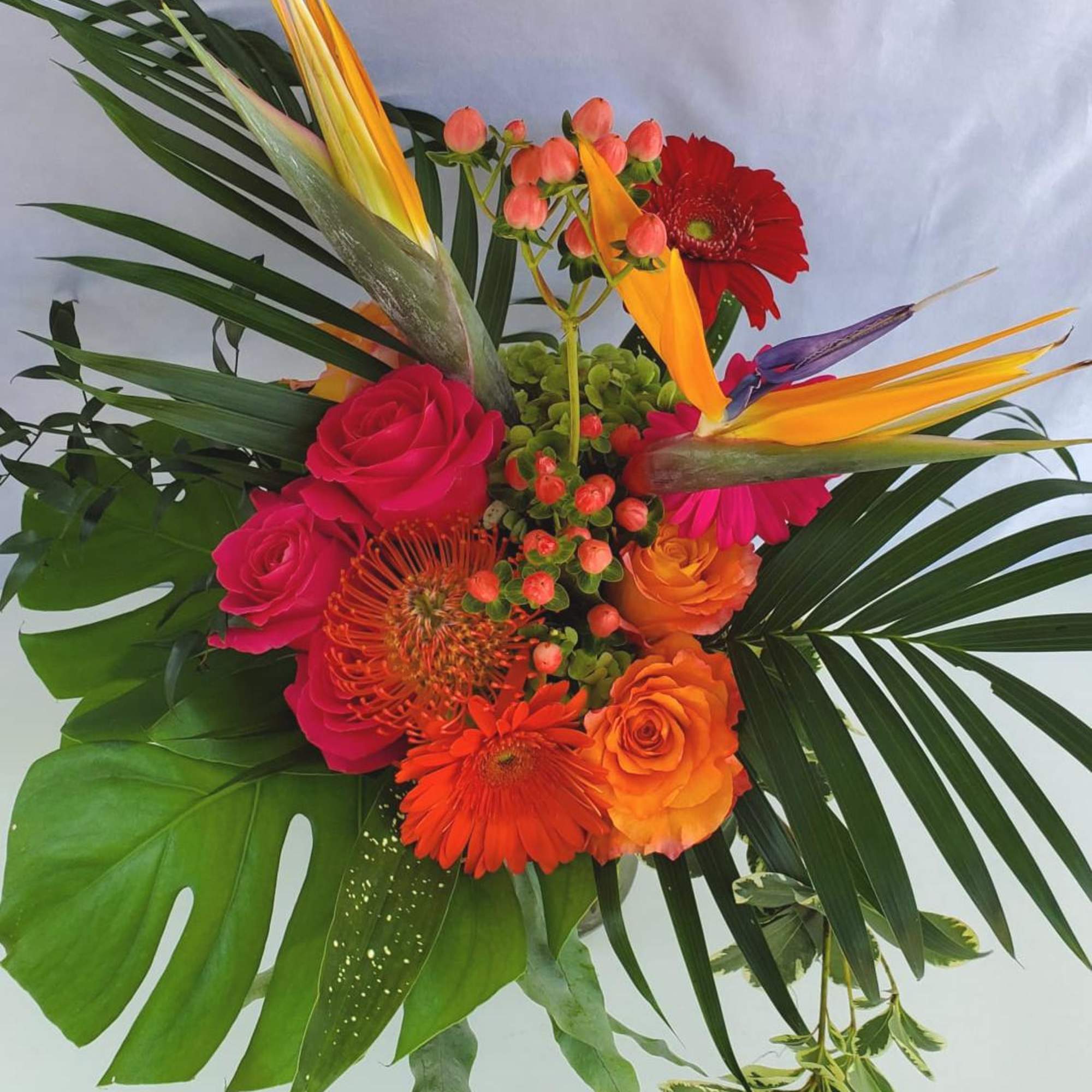 Tropical bouquet with orange and pink blooms, bird of paradise, and bold monstera and palm greenery.