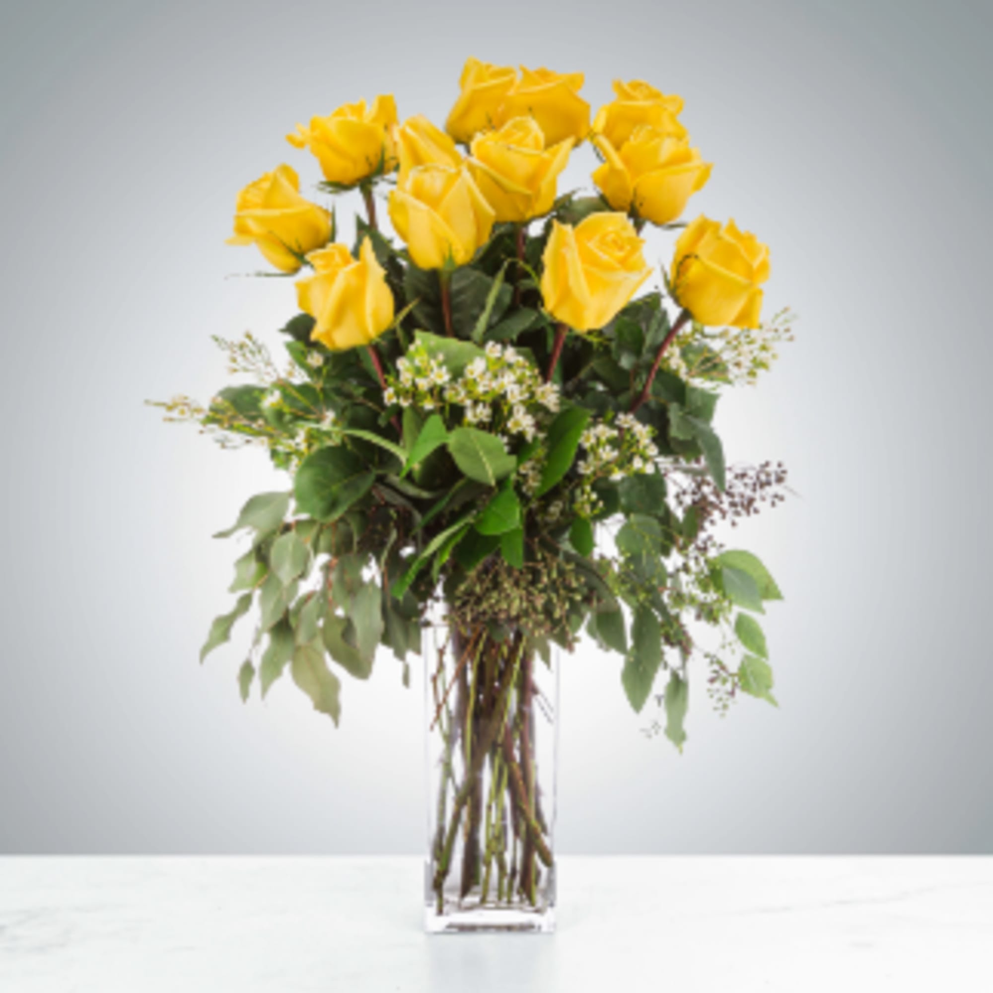 Tall arrangement of yellow roses in a clear rectangular glass vase