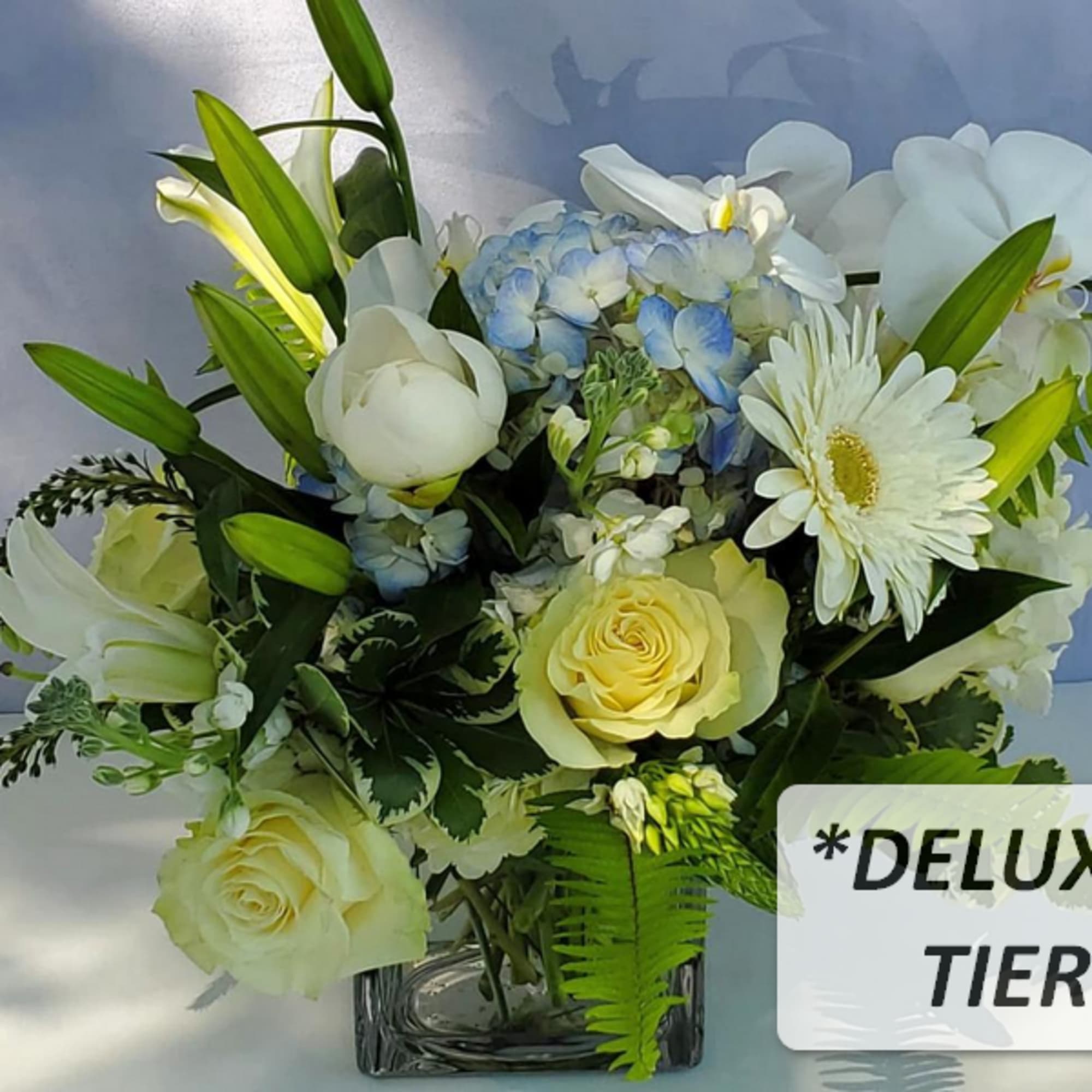 White and pale yellow flower arrangement with blue hydrangea in a clear glass cube vase