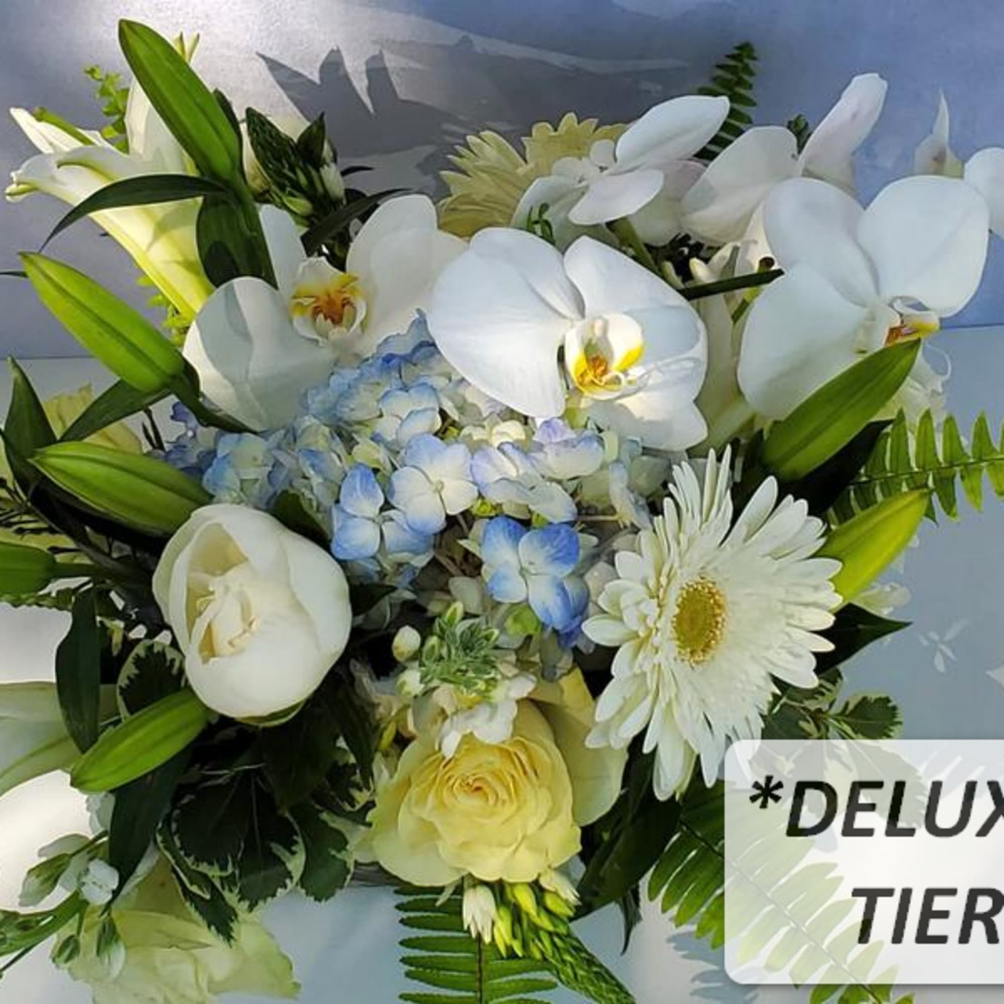 White lilies, orchids, gerbera daisies, yellow roses, and blue hydrangeas in a mixed floral arrangement