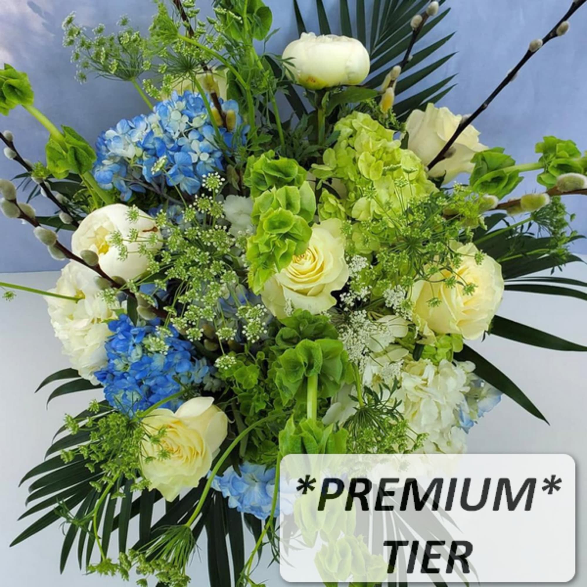 Tall arrangement of cream roses, blue hydrangeas, green bells of Ireland, and palm leaves