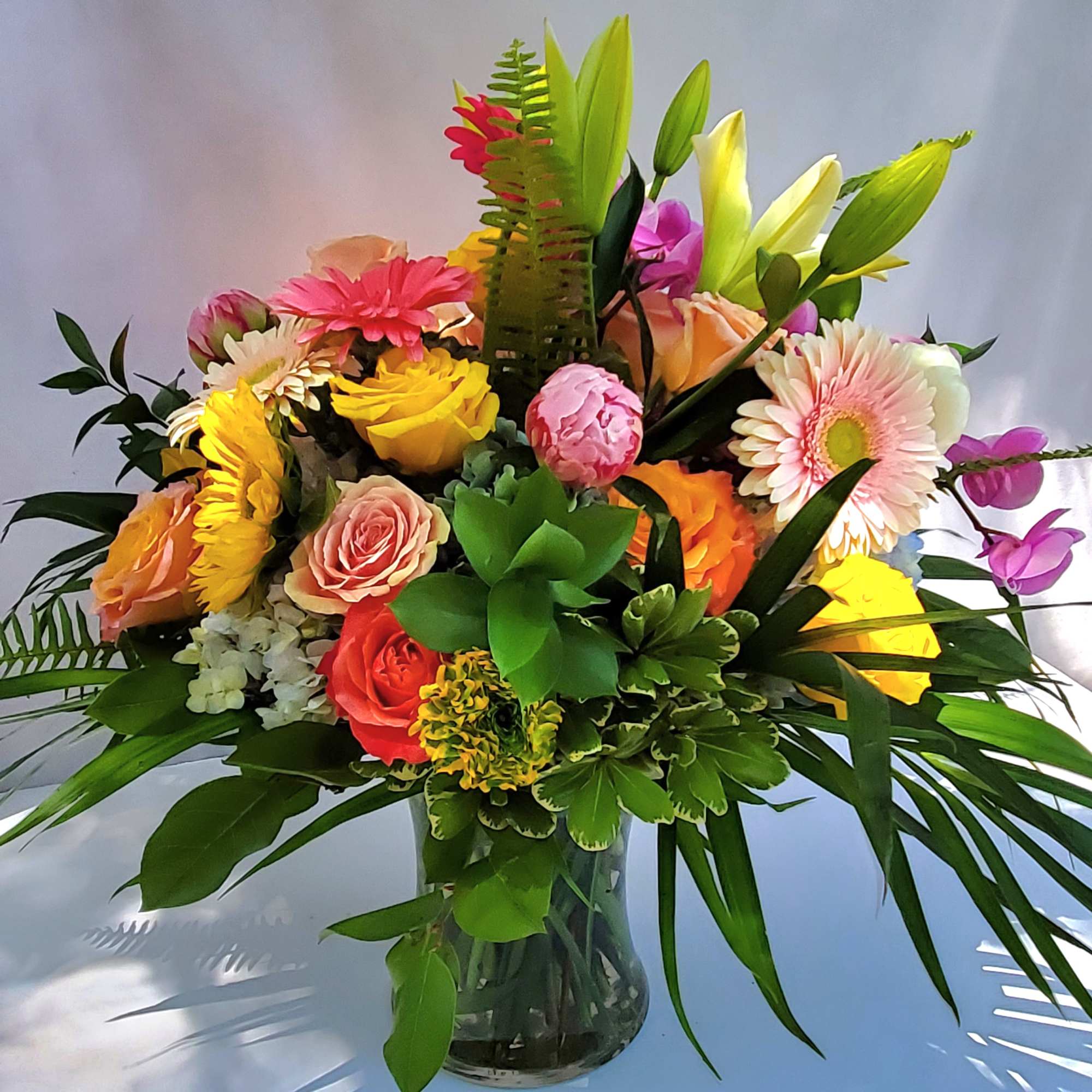 Colorful bouquet of roses, gerbera daisies, lilies, orchids, and succulents in a clear glass vase